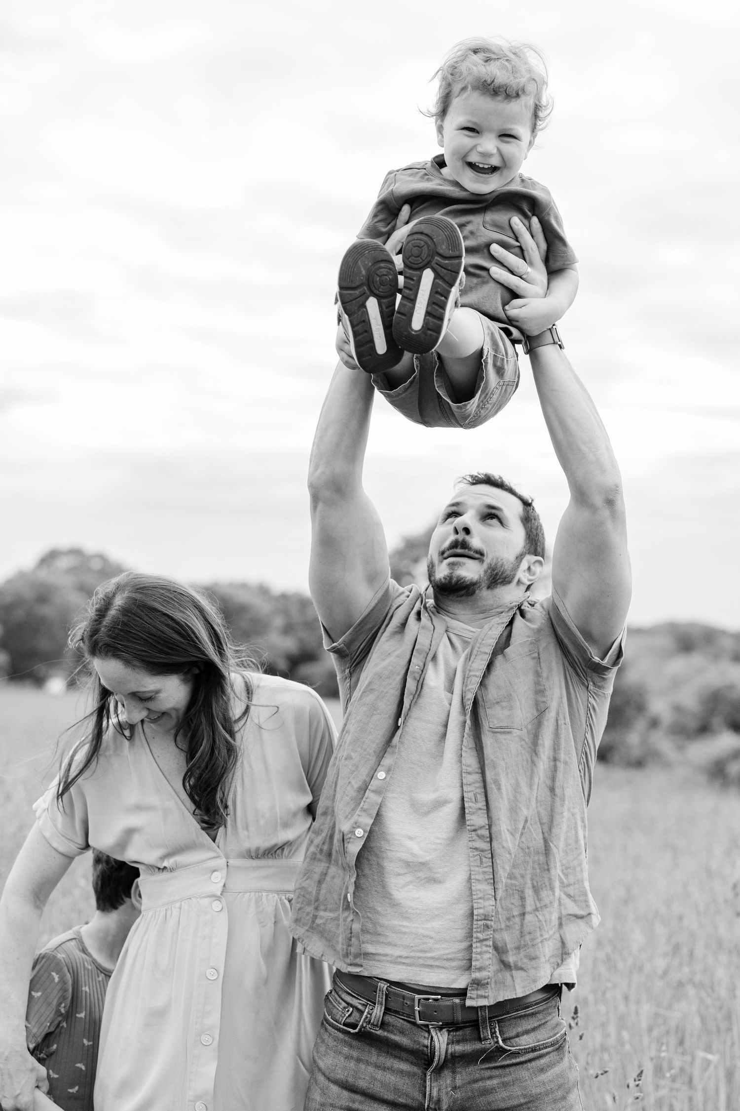 Black and white photo of a family playing and laughing together outdoors in a grassy field on a sunny day.