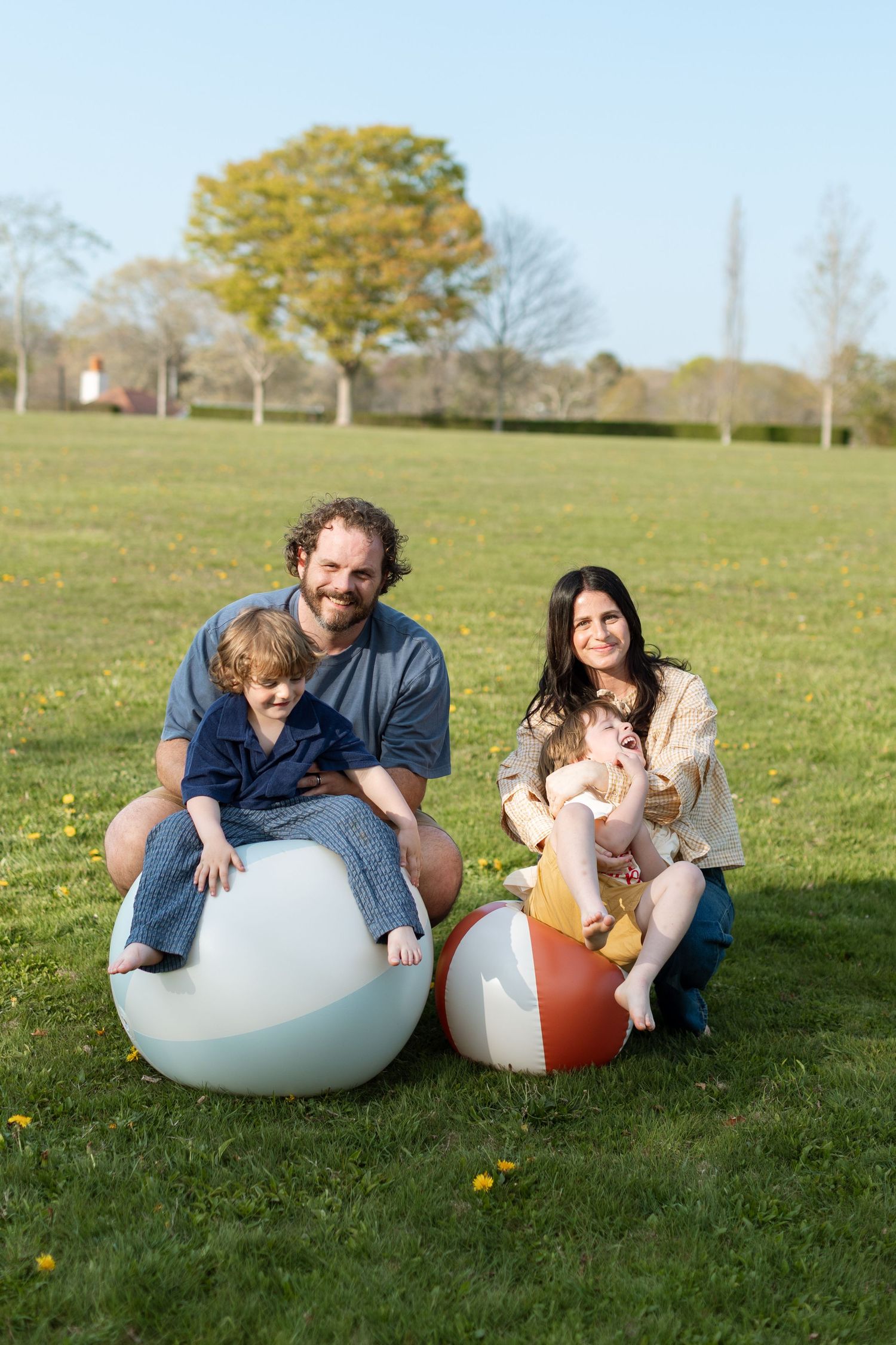 Family lounging playfully on large inflatable spheres in a grassy field on a sunny day.