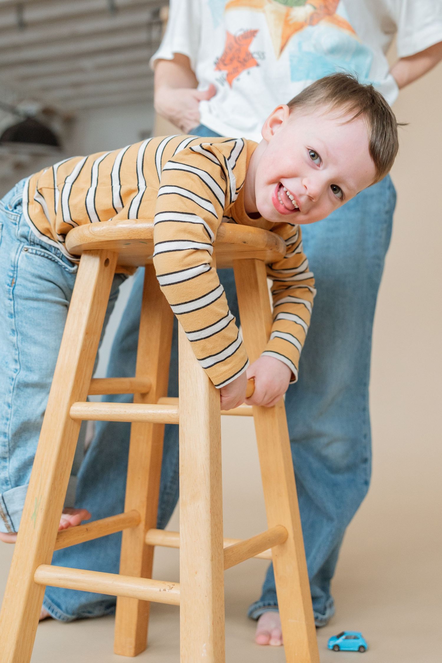 Multiple views show a young child in striped shirt and jeans playing with a wooden high stool while smiling.