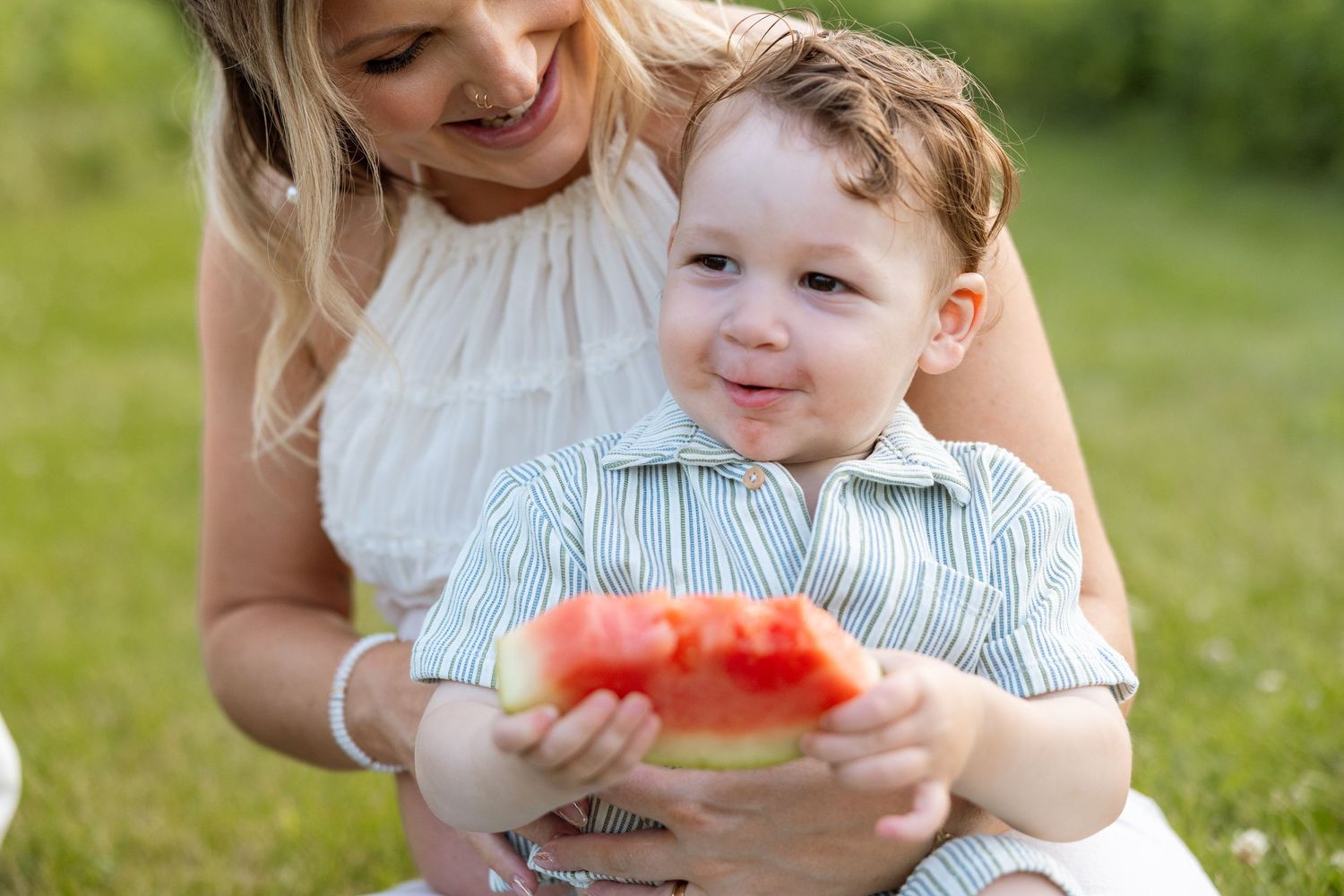 Young child in a striped outfit eats fresh watermelon outdoors on a sunny summer day.