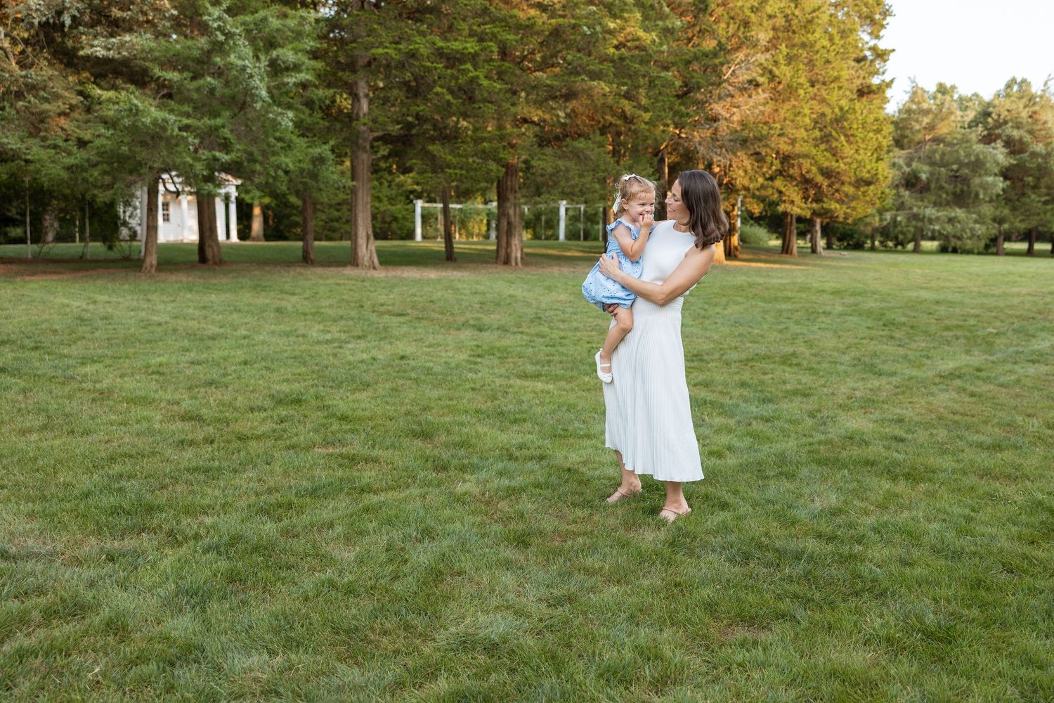 A couple wearing white takes golden hour maternity photos on a lush grassy lawn in late summer.