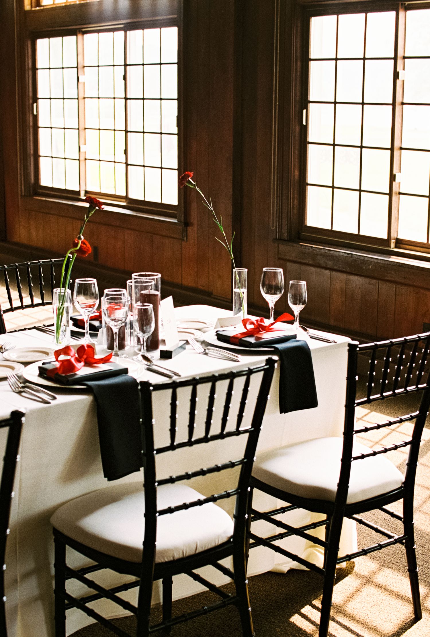 Intimate wedding table setting with black chairs and white linens near sunlit windows.