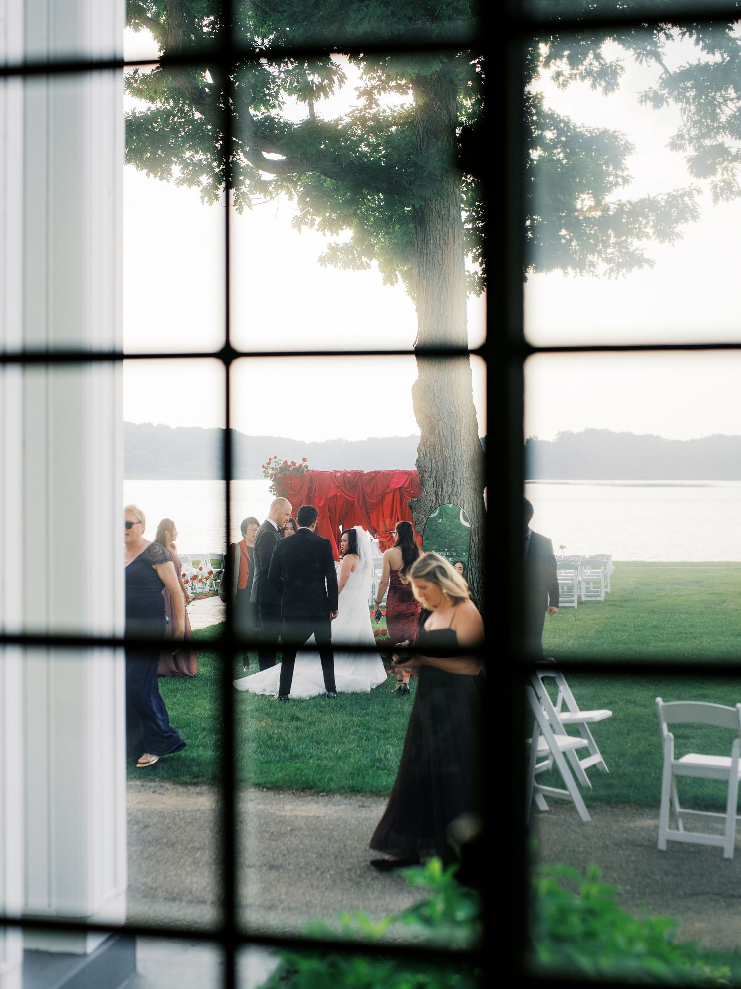 Wedding ceremony setup viewed through window panes with waterfront view.