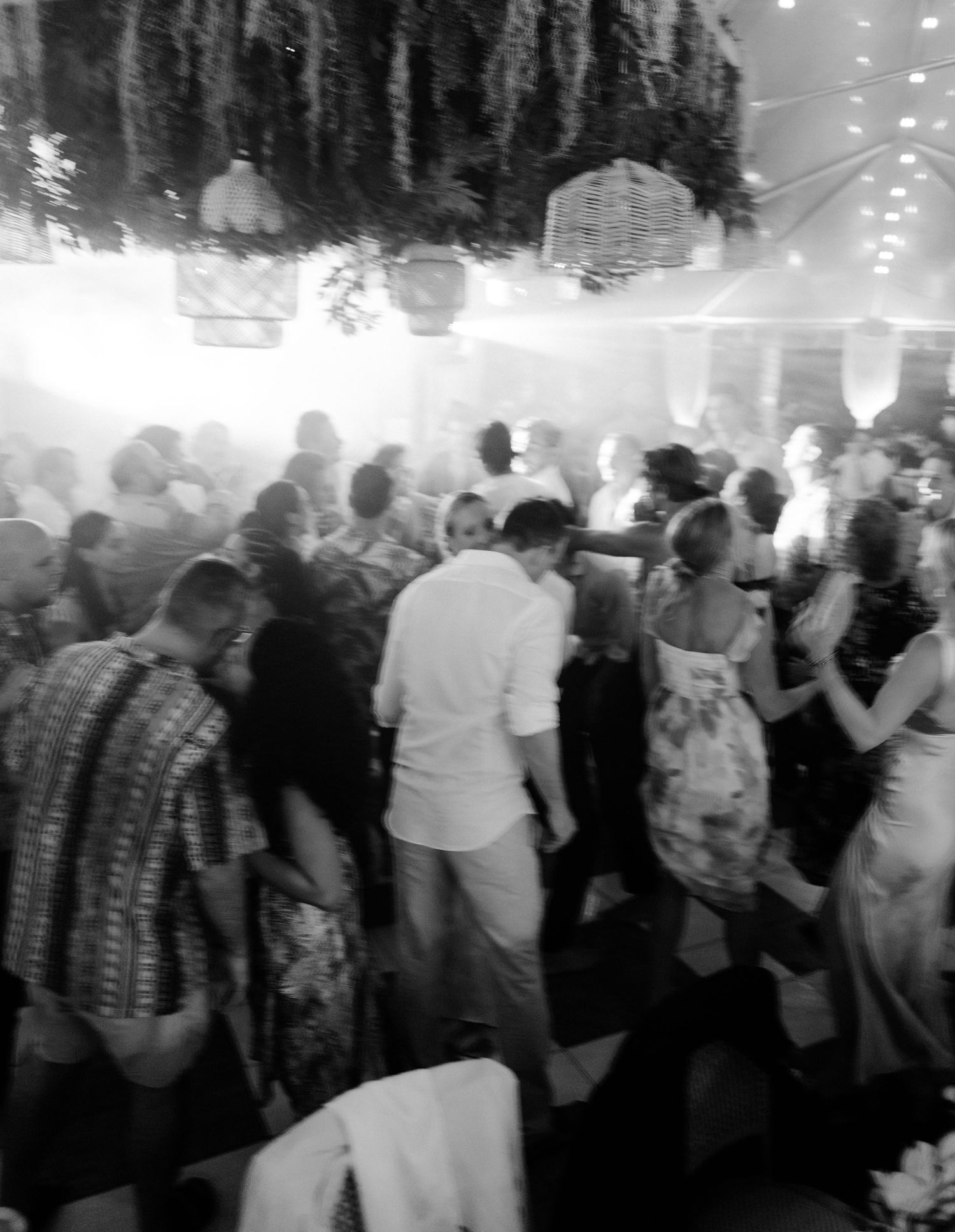 A crowded dance floor filled with people celebrating at an indoor event with ambient lighting.
