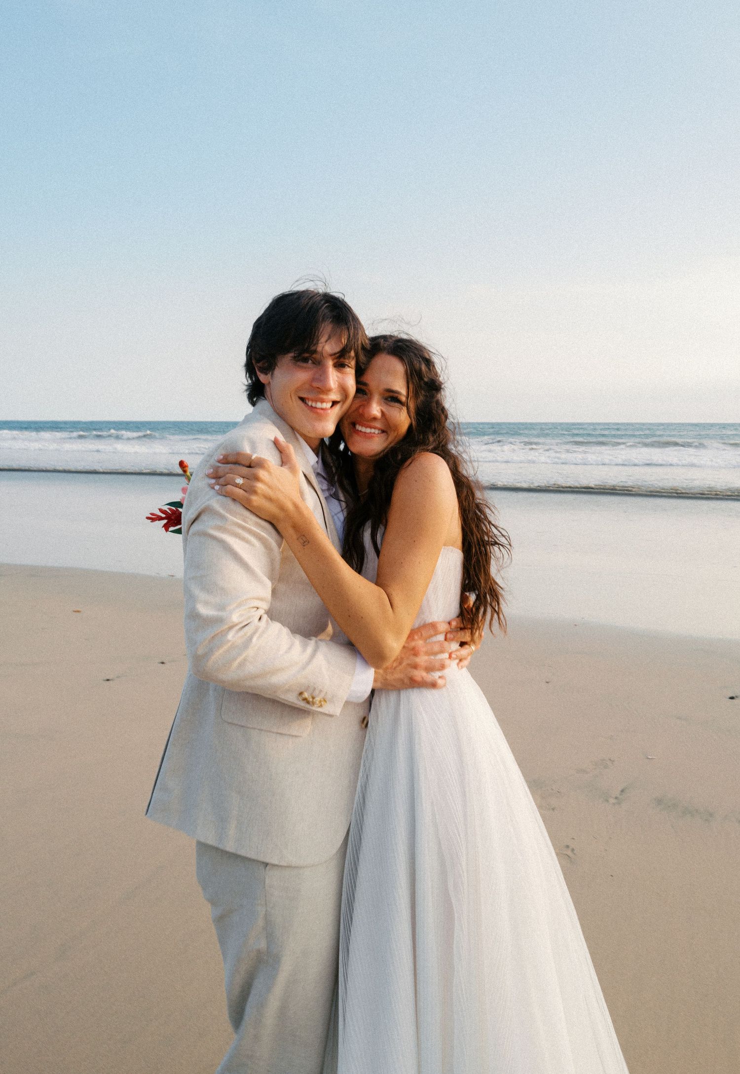 A couple shares an intimate moment while dancing together on a sunny beach.