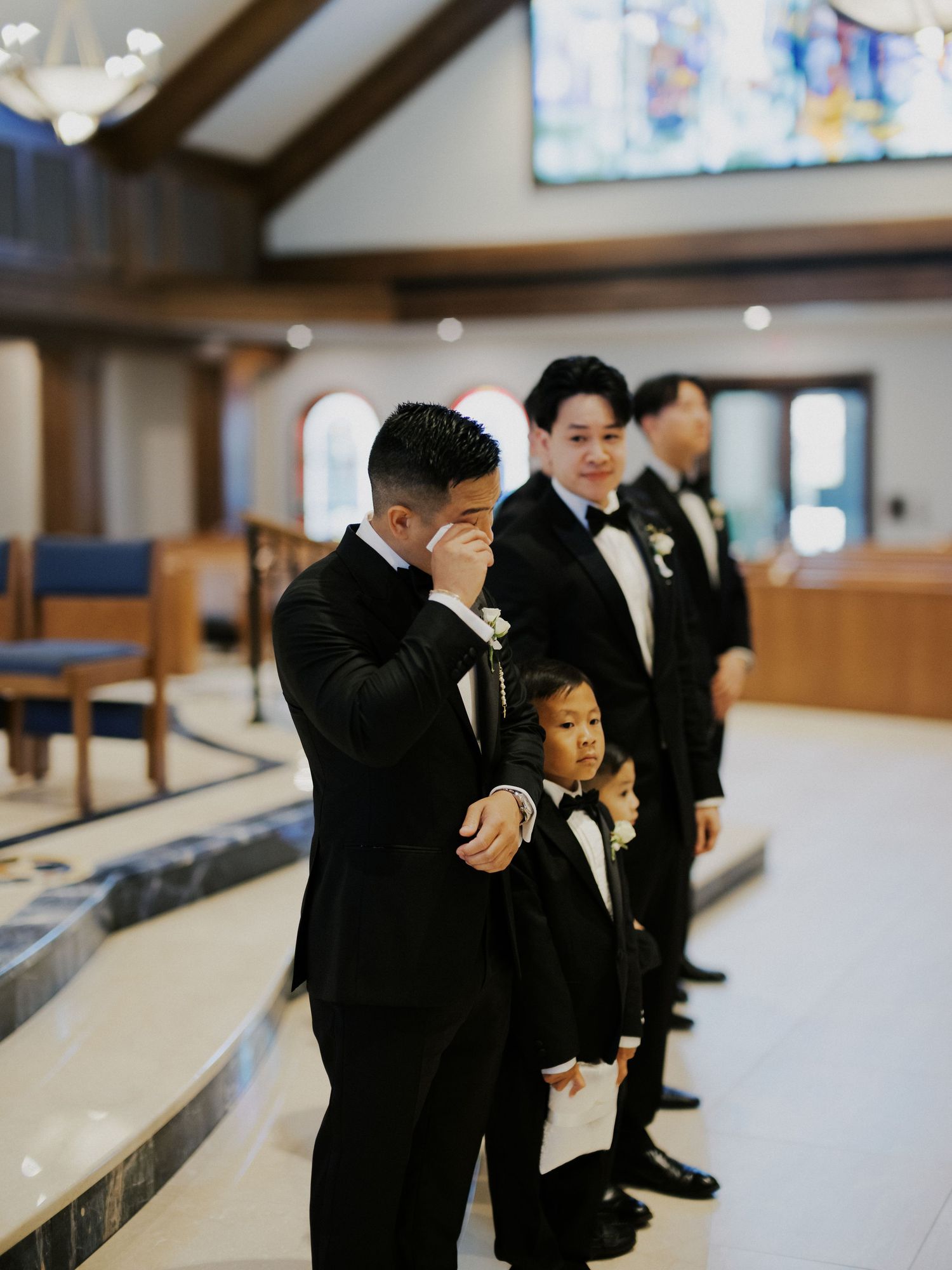 Wedding party groomsmen in black suits celebrate and cheer while standing in a bowling alley lane.