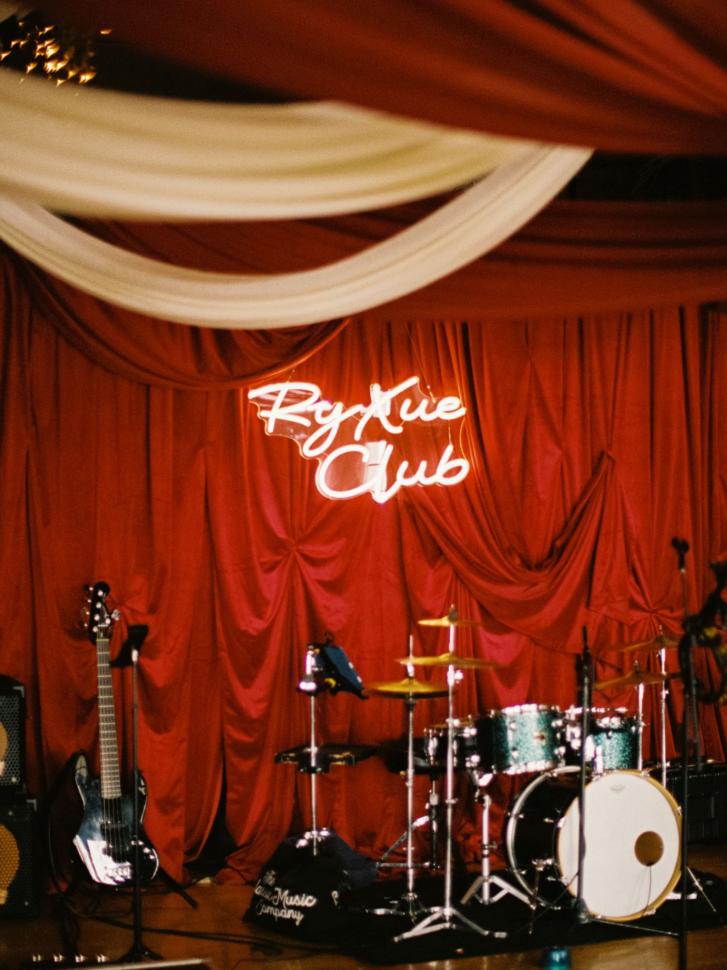 Musical stage setup with drum sets and equipment against red draped backdrop.