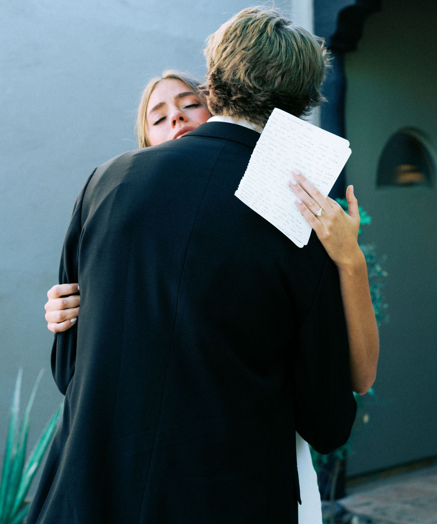 A couple embraces emotionally while holding papers during what appears to be a private moment.