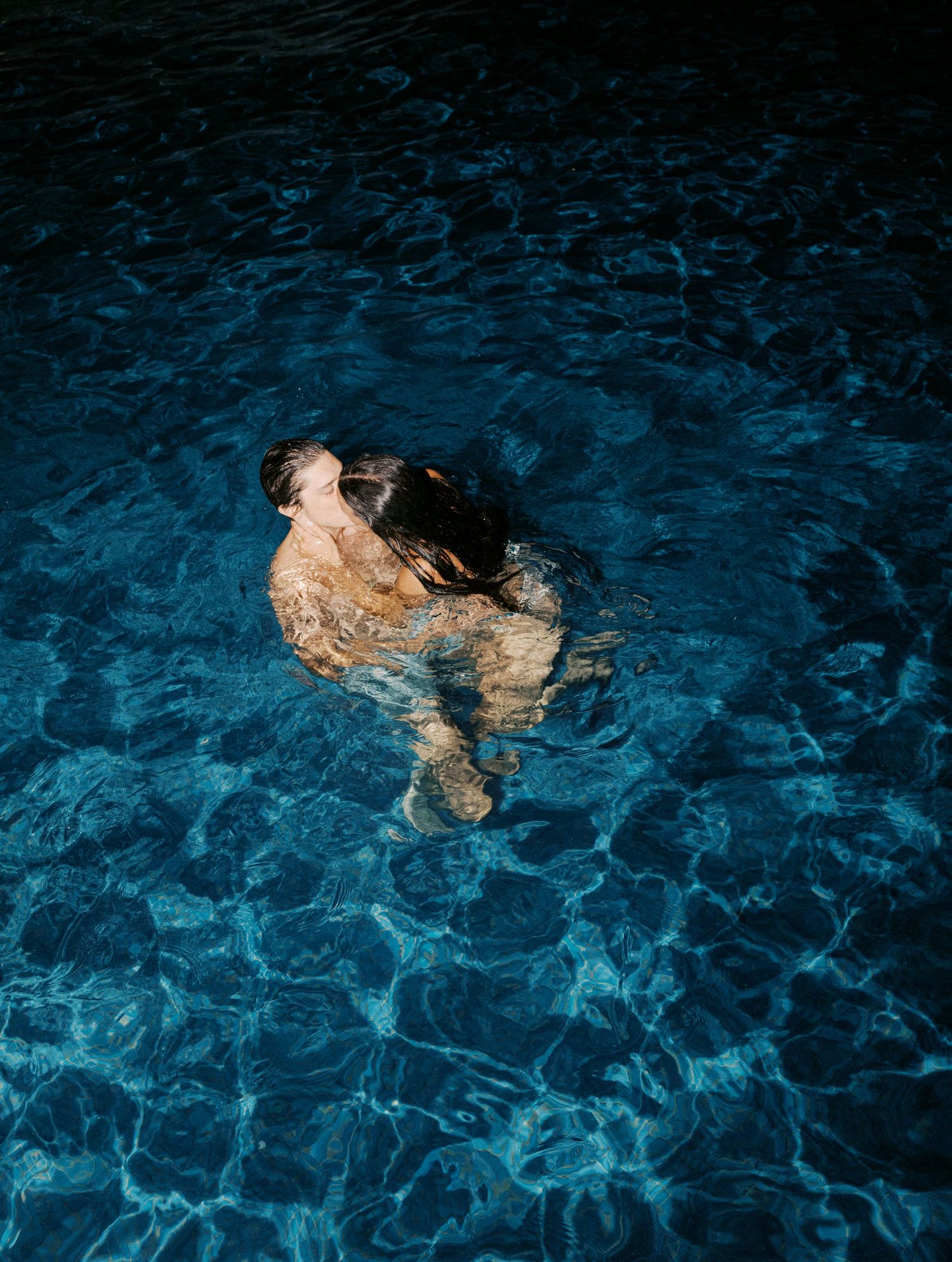 Person swimming in dark blue illuminated pool water at night.