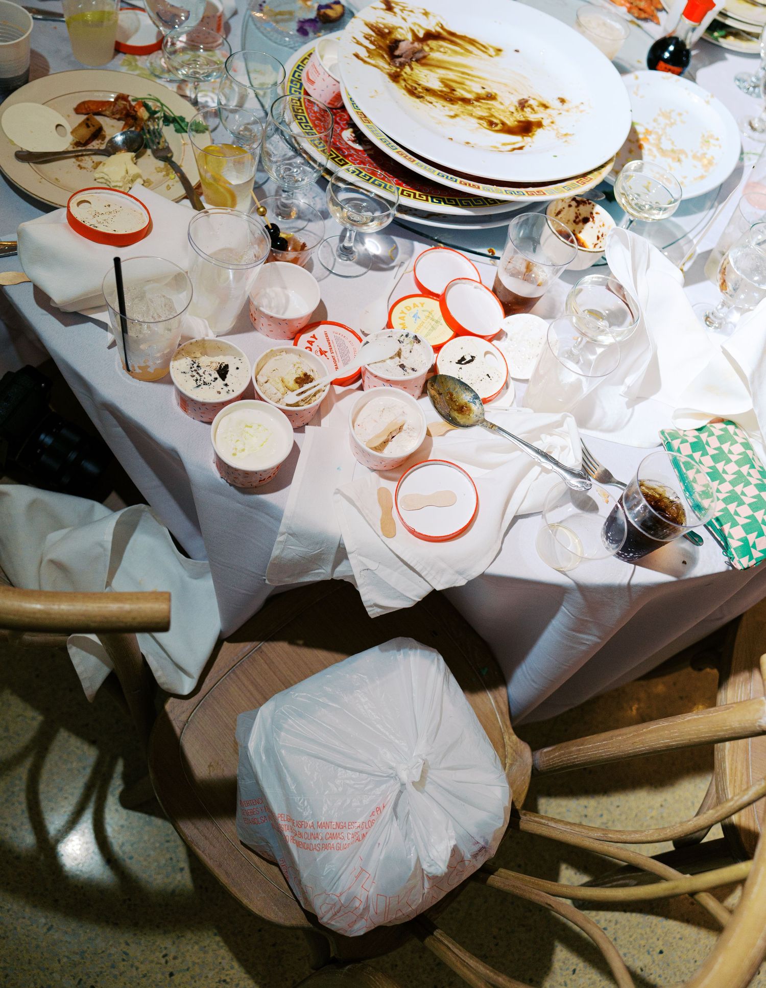 Aftermath of a wedding reception showing empty plates and scattered decorations on white tablecloths.