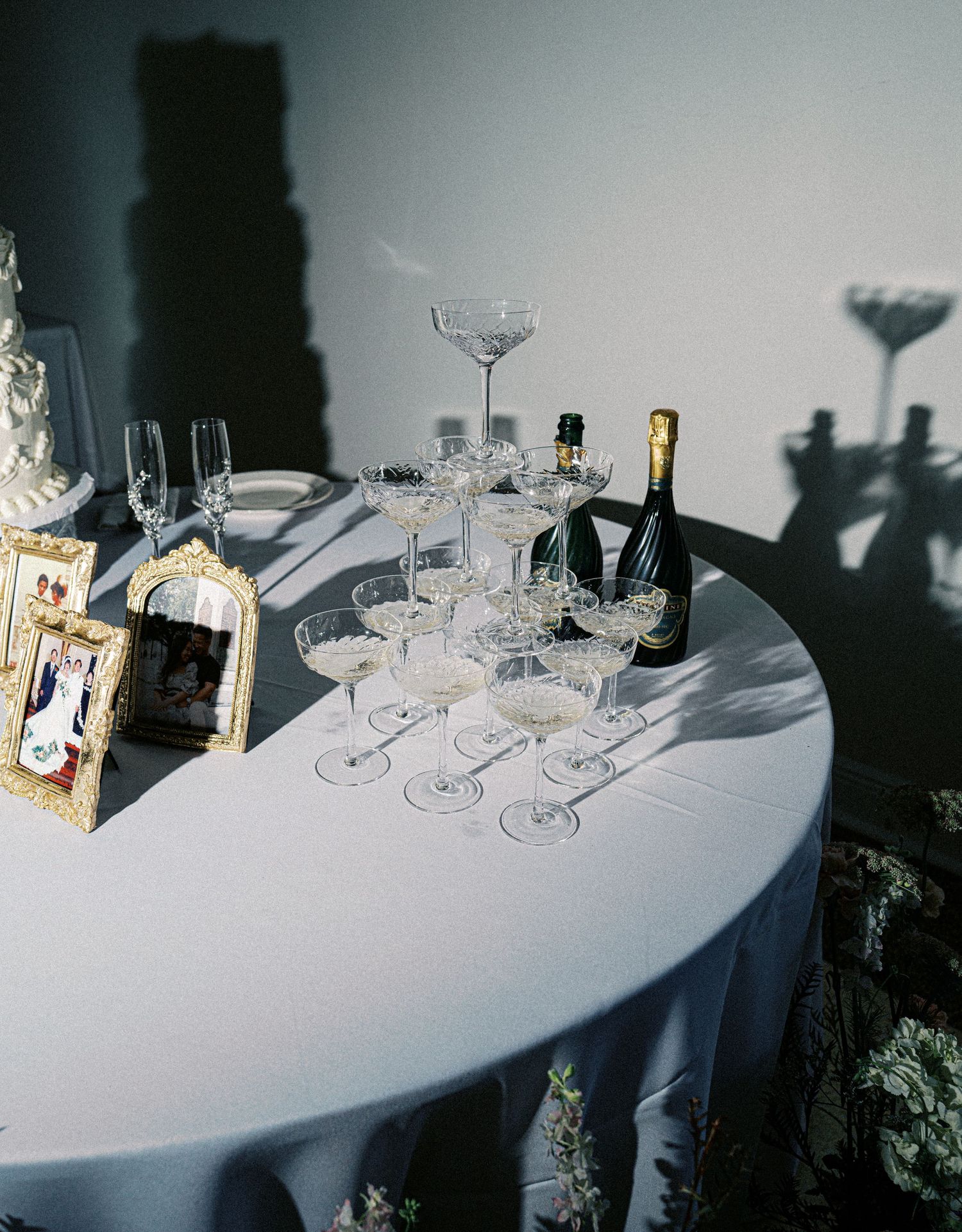 Elegant table setting with champagne glasses and bottles arranged on a white tablecloth with dramatic shadows.