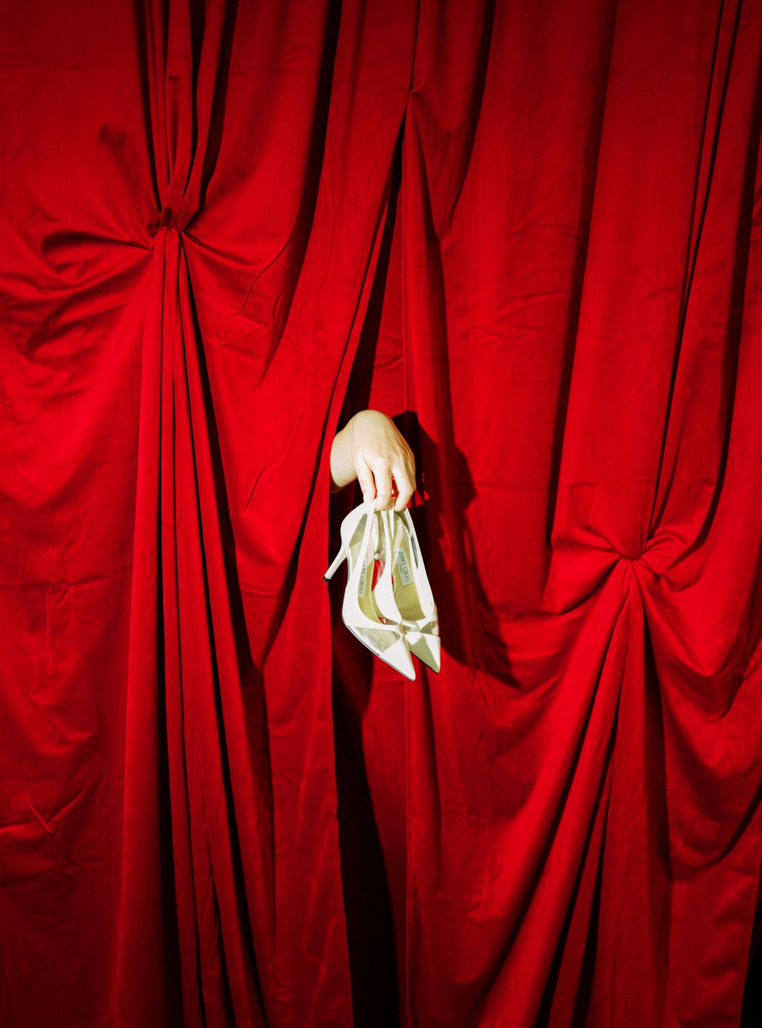 Dramatic red theater curtains with a hand reaching through the folds in dramatic lighting.