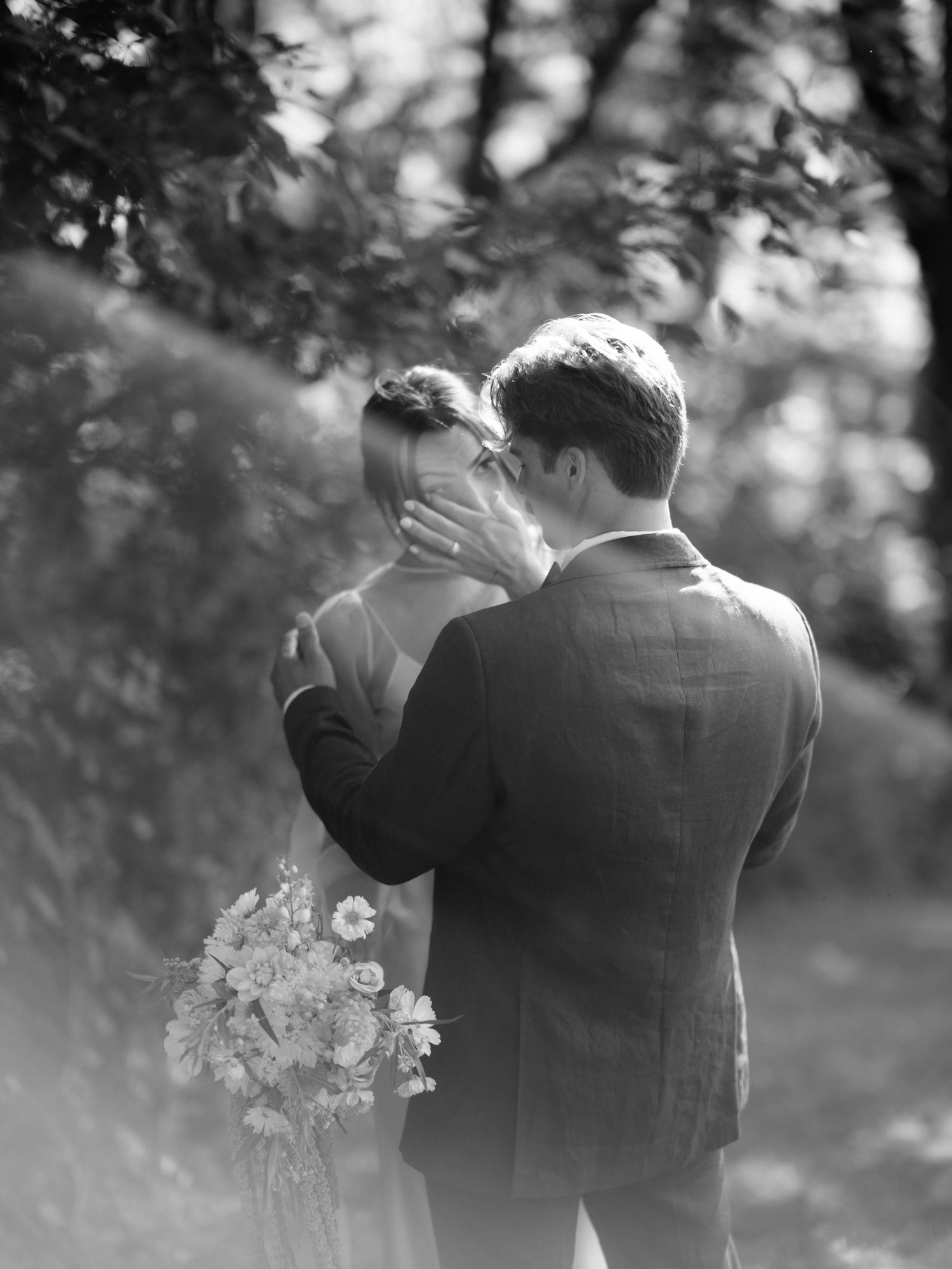 Black and white romantic portrait of couple embracing outdoors among flowers.