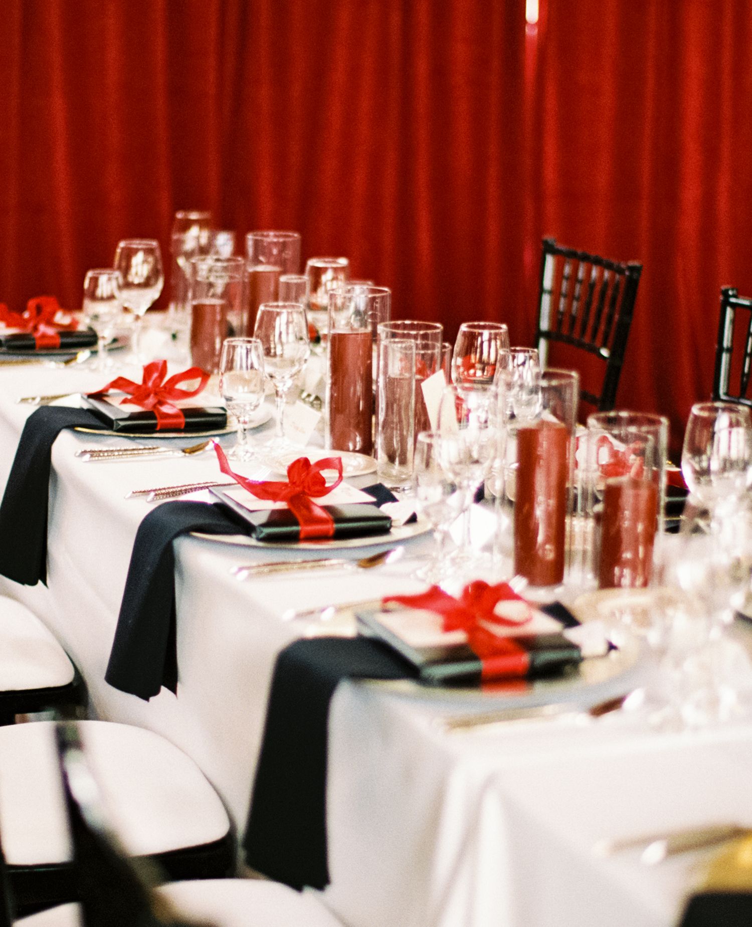 Elegant table settings at a formal event with white tablecloths, black napkins, and red bow accents.