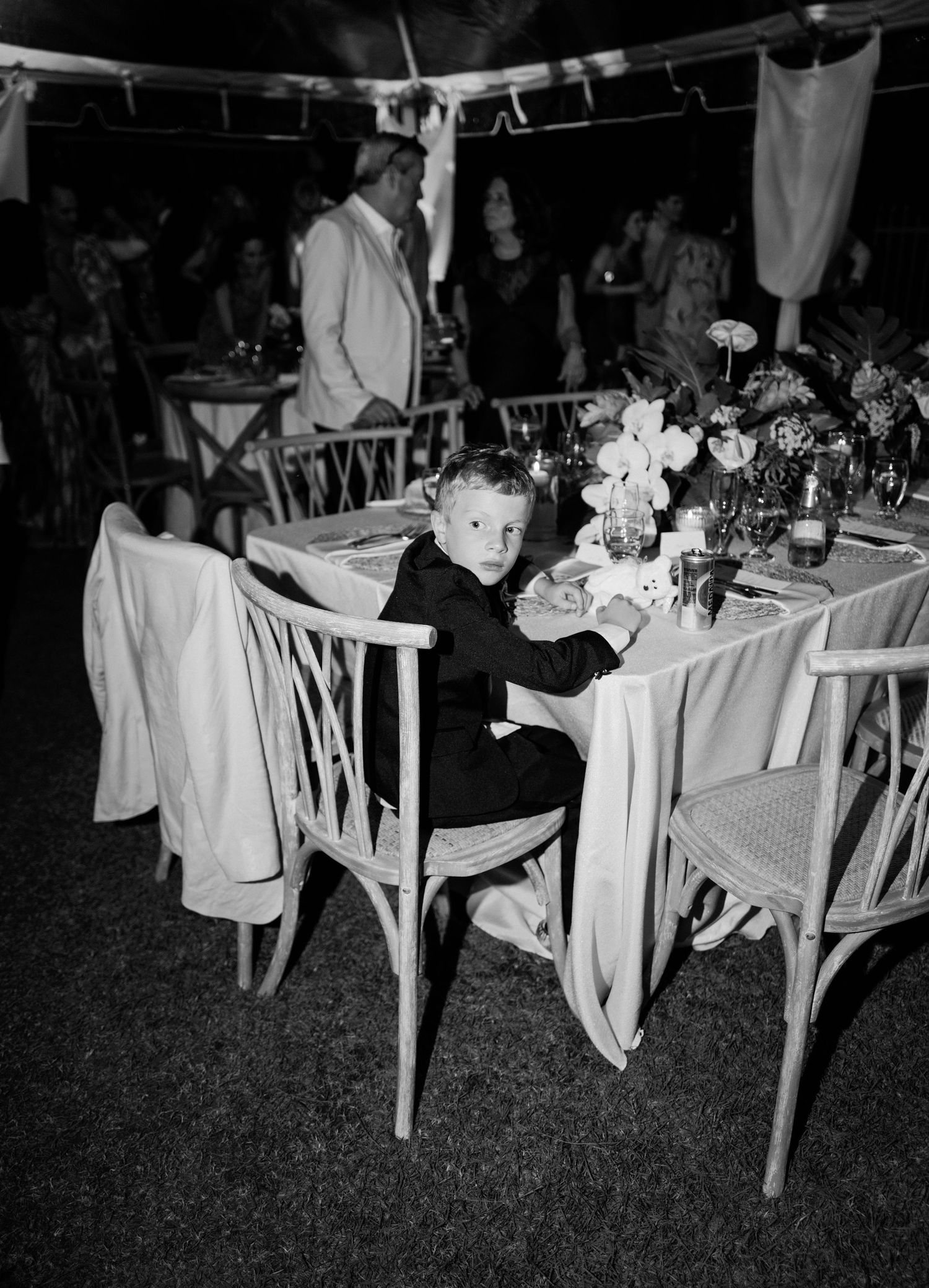 Elegant outdoor wedding reception tables with white linens and floral centerpieces arranged on a lawn at dusk.