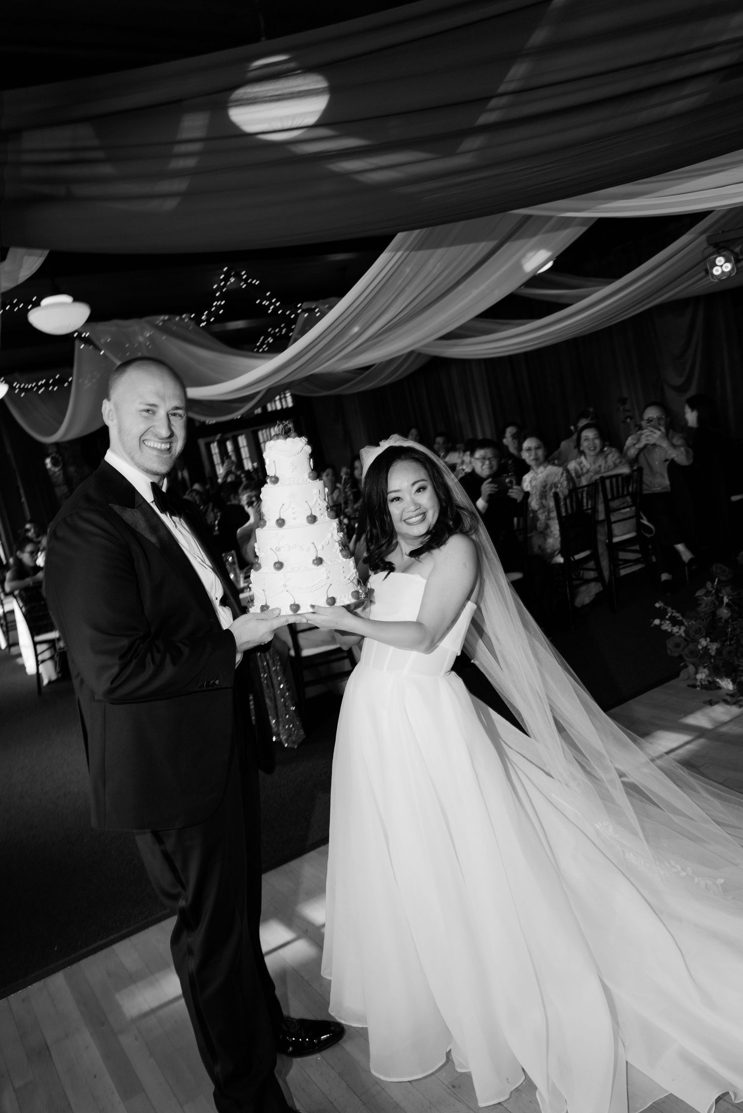A couple holds their elegant white wedding cake at their reception.