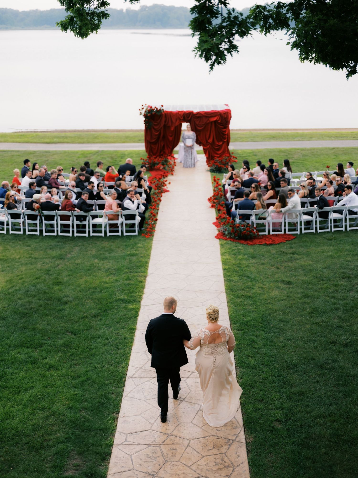 Outdoor wedding ceremony setup with red arch and white chairs overlooking a serene lake.