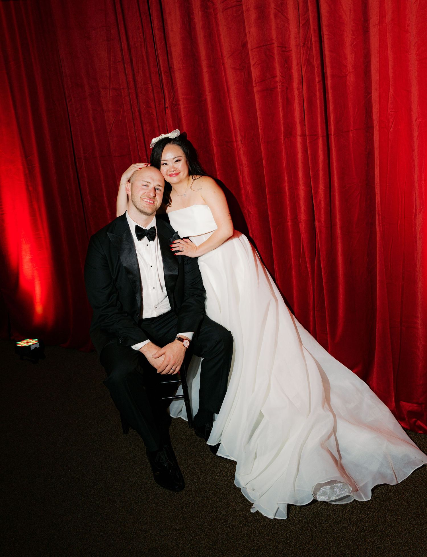 A couple poses for portraits against a dramatic red curtain backdrop.