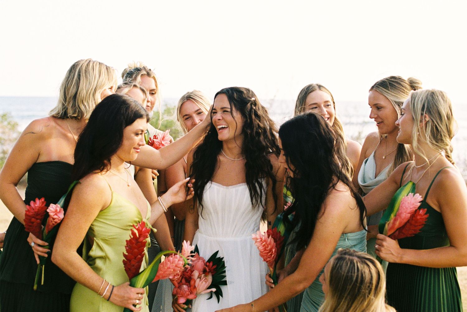 Bridesmaids in colorful dresses laughing and celebrating together during outdoor wedding festivities.