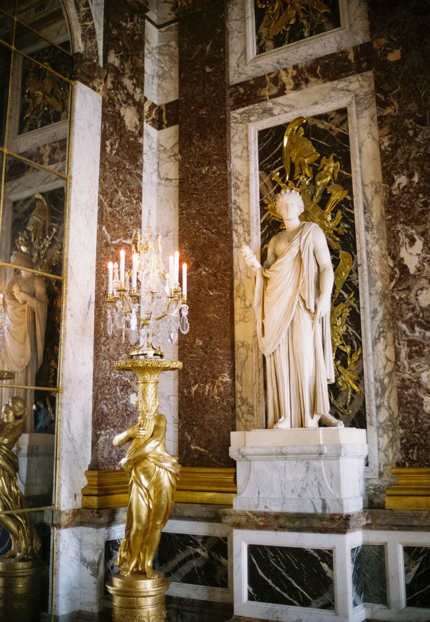 Ornate marble statues and chandeliers line the Hall of Mirrors in the Palace of Versailles, France.