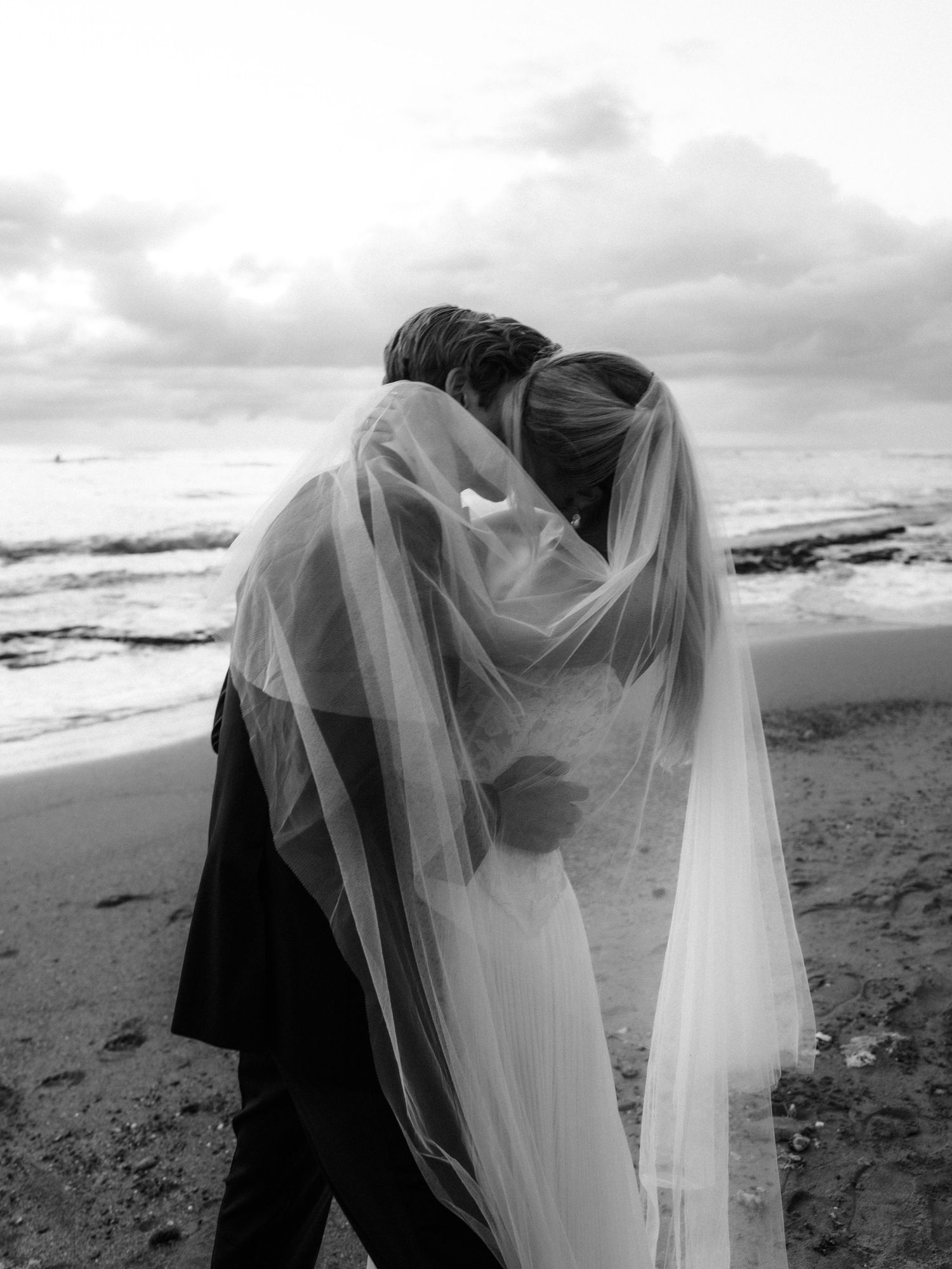 A romantic black and white sequence of a couple embracing on a beach with a flowing veil in the wind.
