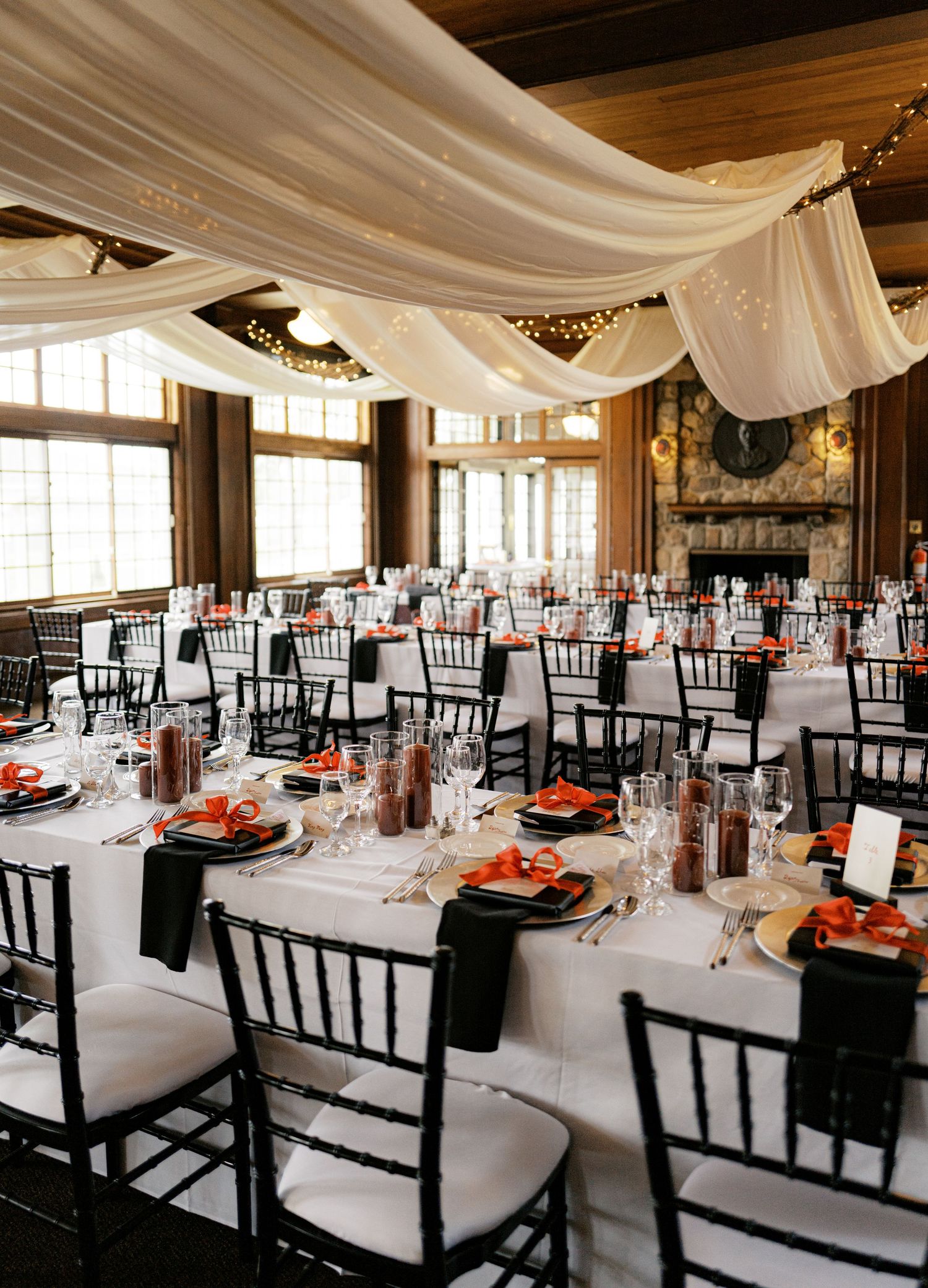 Elegant wedding reception venue with white tablecloths, black chairs, and draped fabric ceiling decorations.