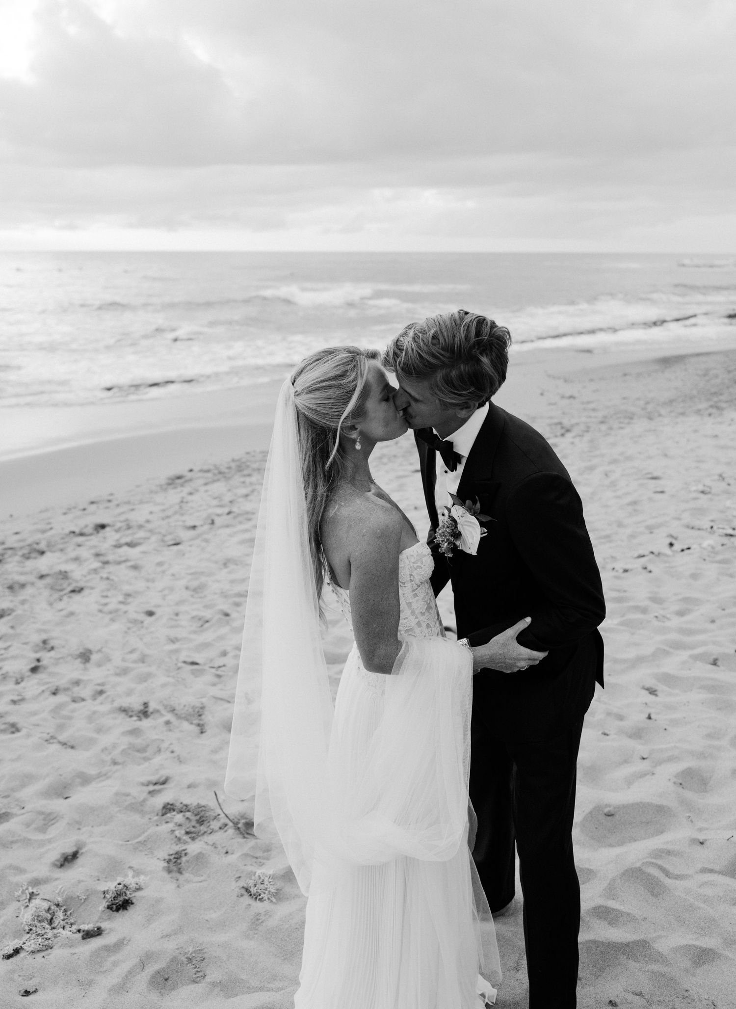 A romantic black and white beach wedding photo showing a couple sharing an intimate moment on a sandy shore.