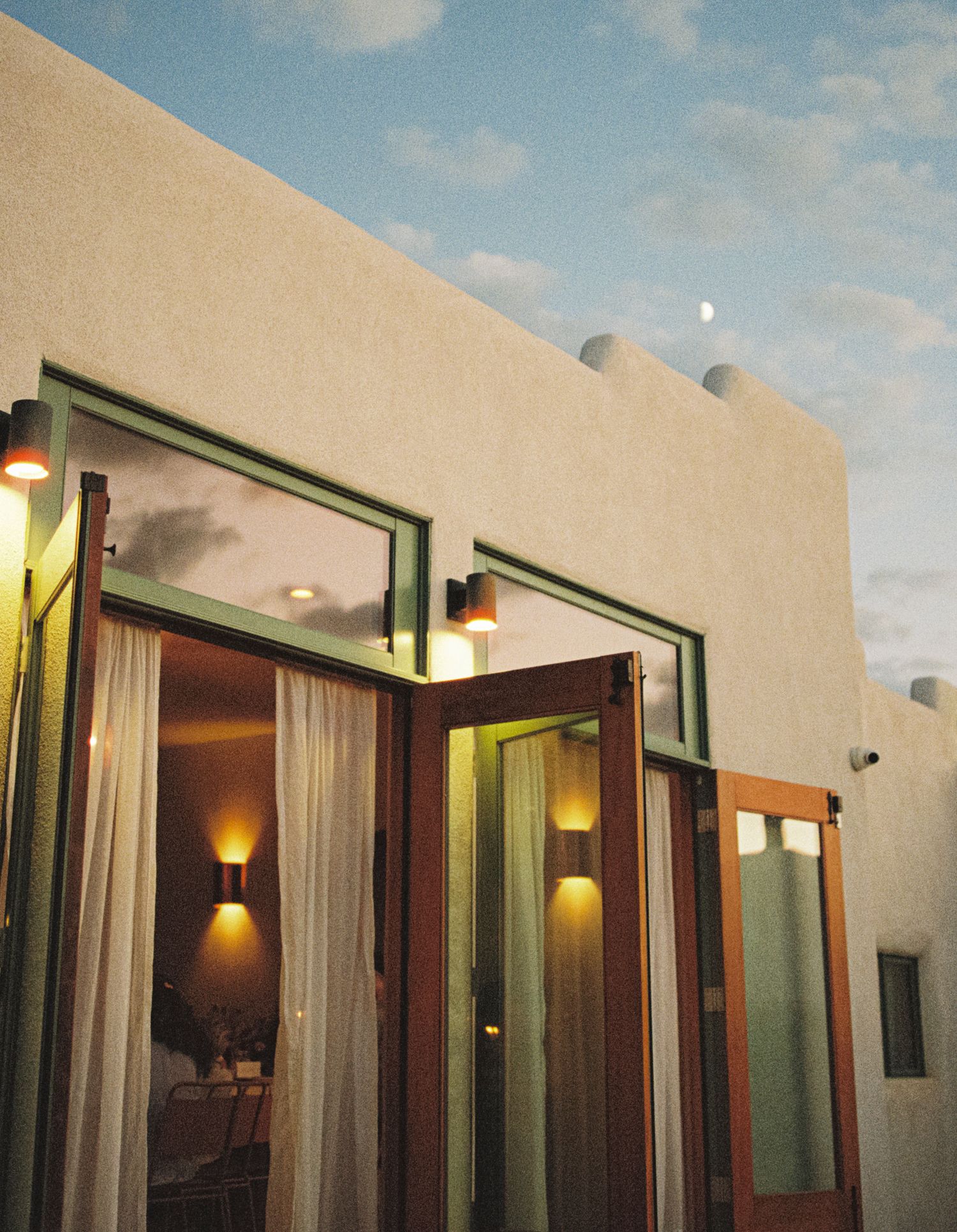 Modern adobe-style building exterior with glass doors and warm lighting at dusk, featuring southwestern architectural elements.