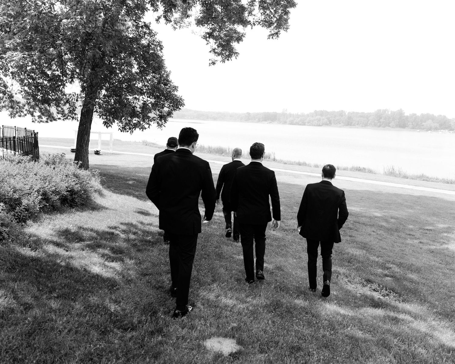 Three silhouettes walk together along a grassy path beside a lake in black and white.