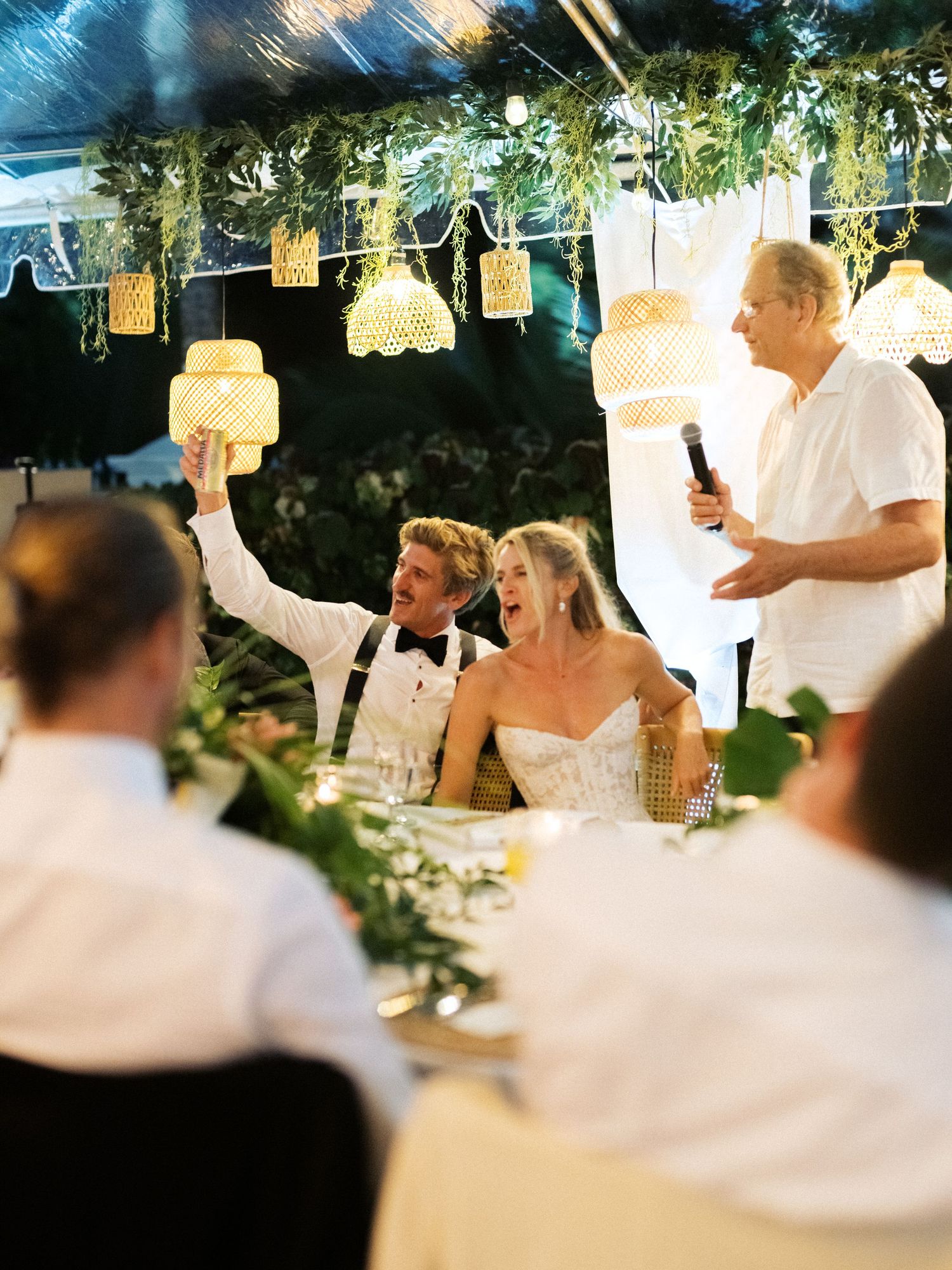 People gathered at an outdoor dinner party under string lights and greenery decorations at dusk.