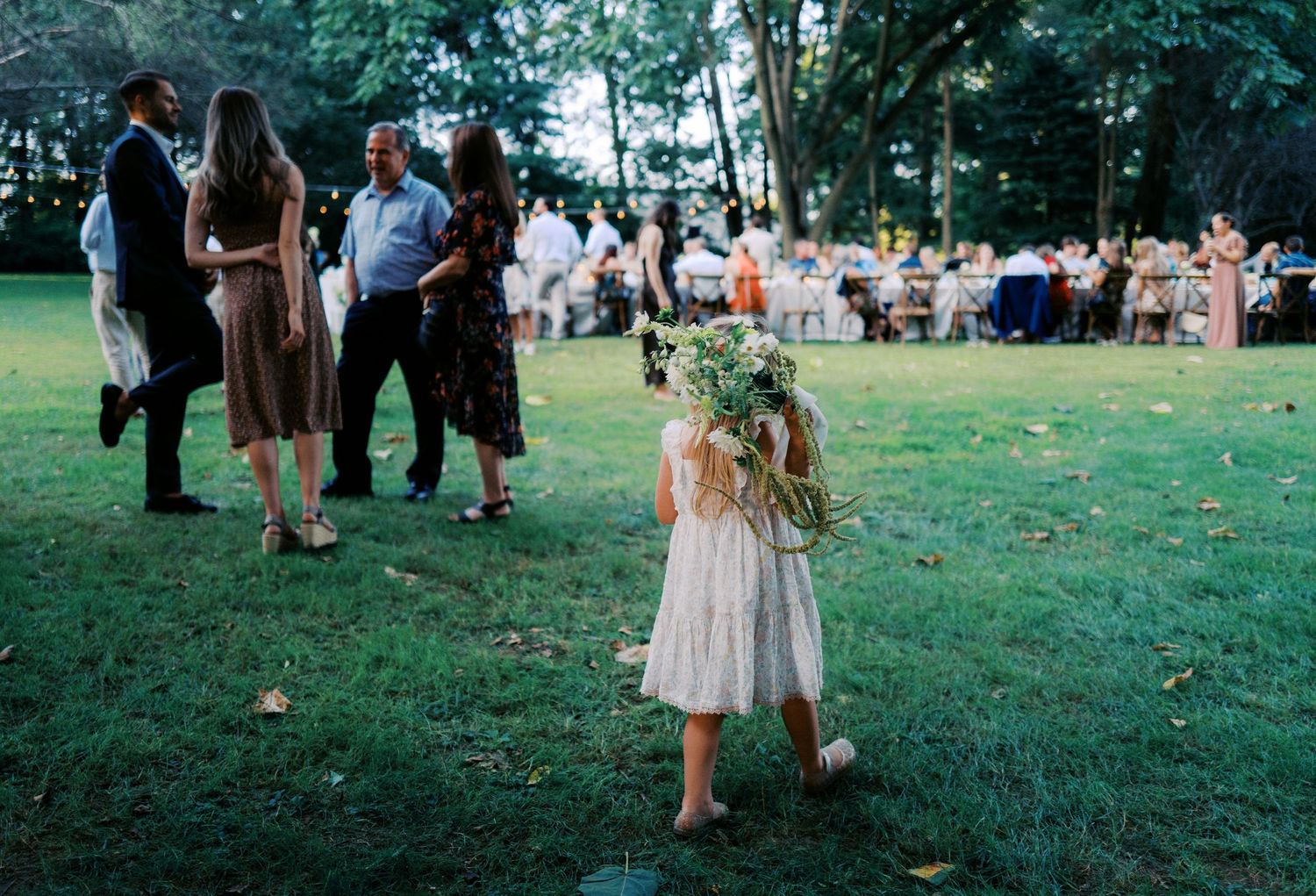 Wedding guests gather on a lush green lawn during an outdoor summer celebration.