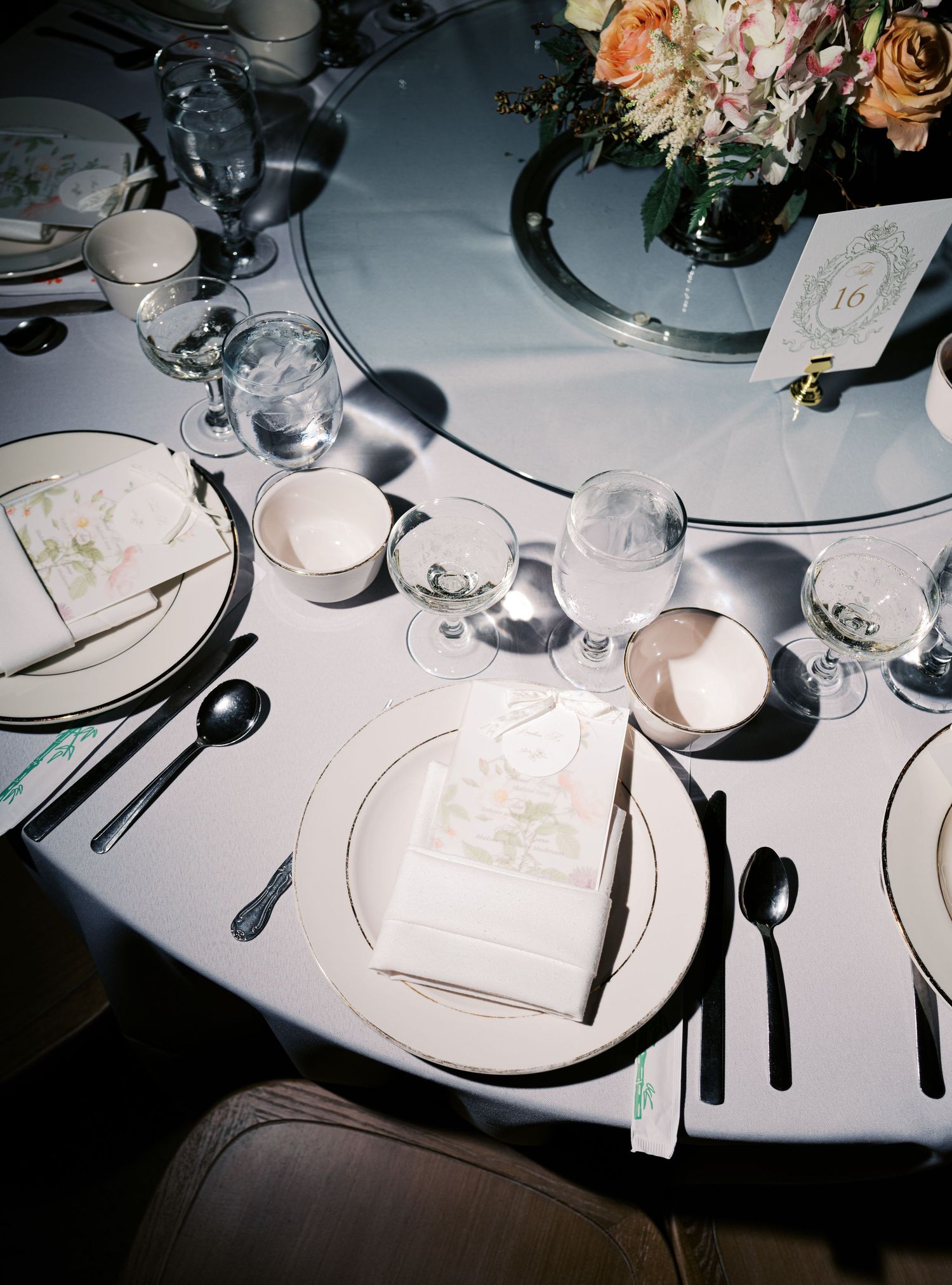 Elegant wedding reception table settings with white linens, floral centerpieces, and formal place settings in dramatic lighting.
