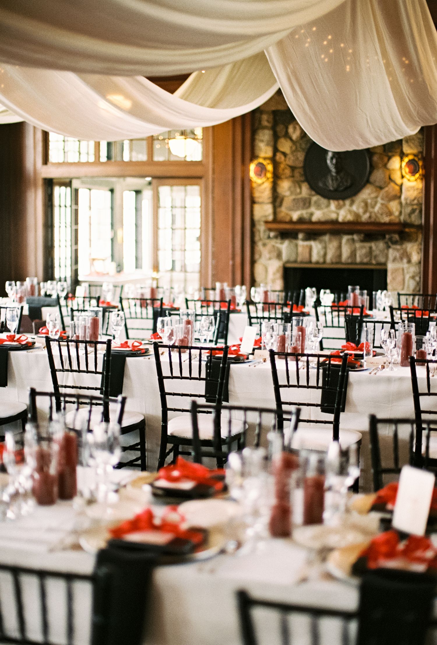 Wedding reception hall with white draping, stone fireplace and formal table settings.