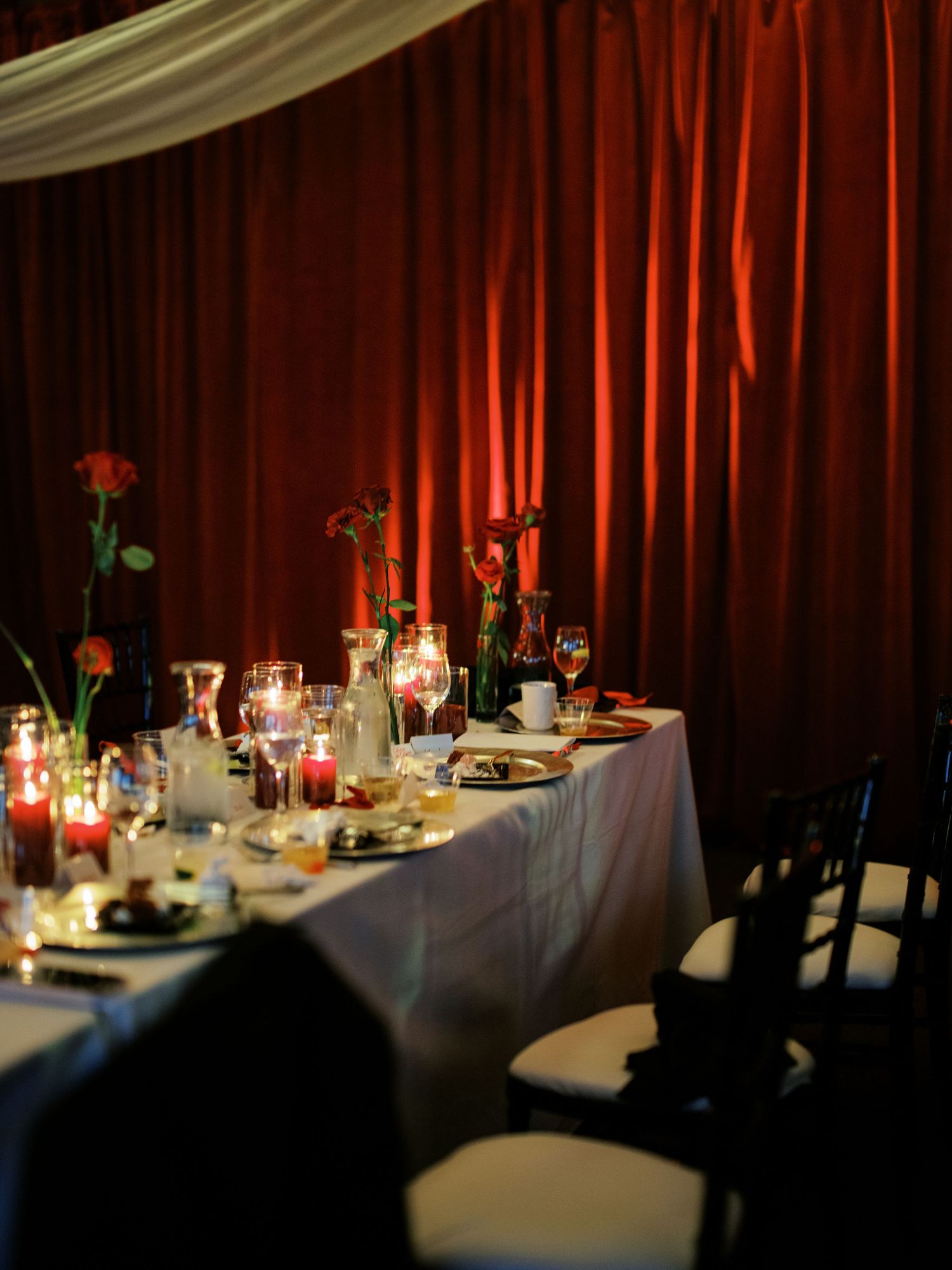 Elegant wedding reception tables set with glowing candles and dark red drapery creating an intimate atmosphere.