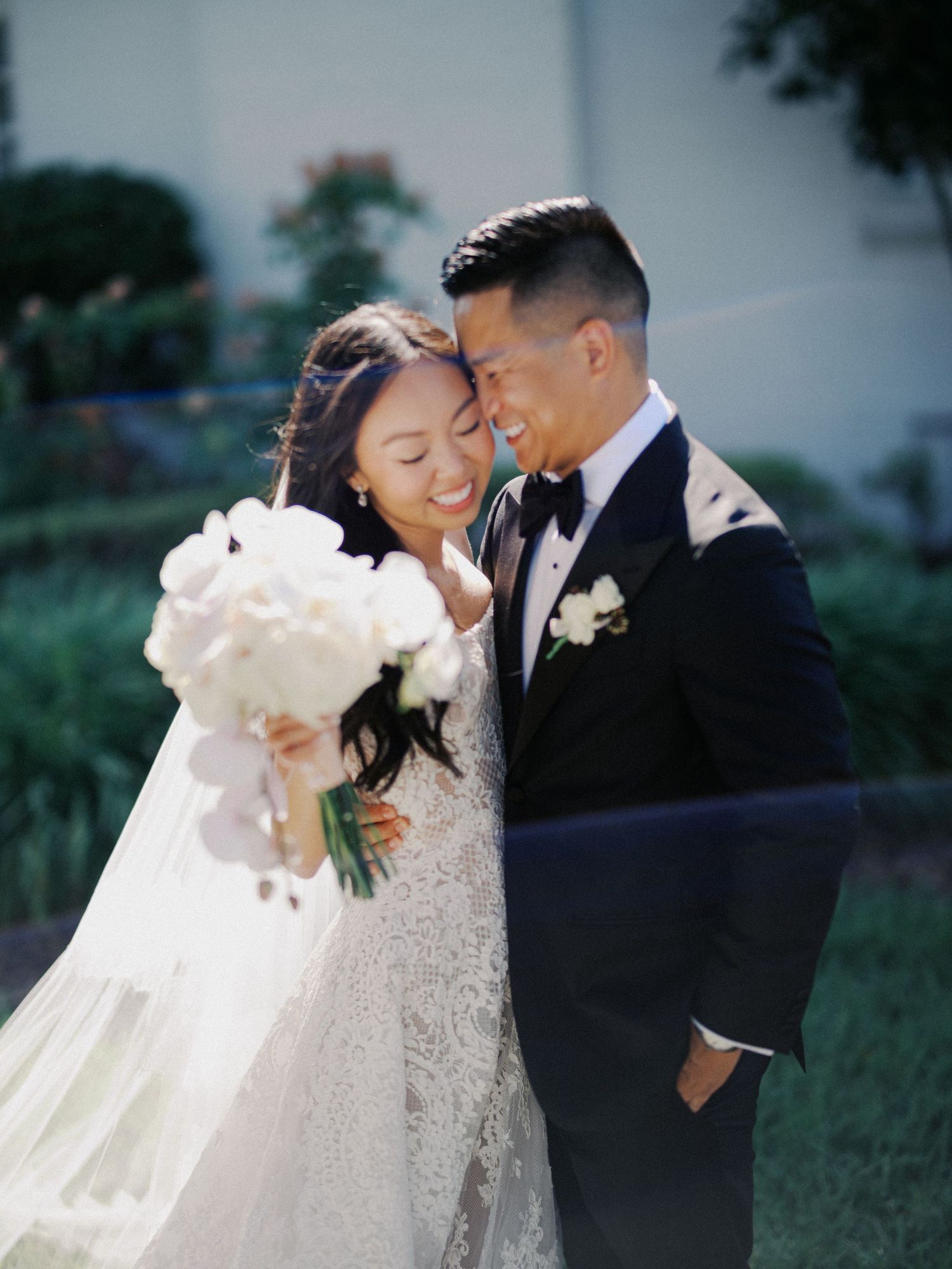A romantic outdoor wedding photoshoot featuring a couple in elegant attire with a flowing white veil catching the breeze.
