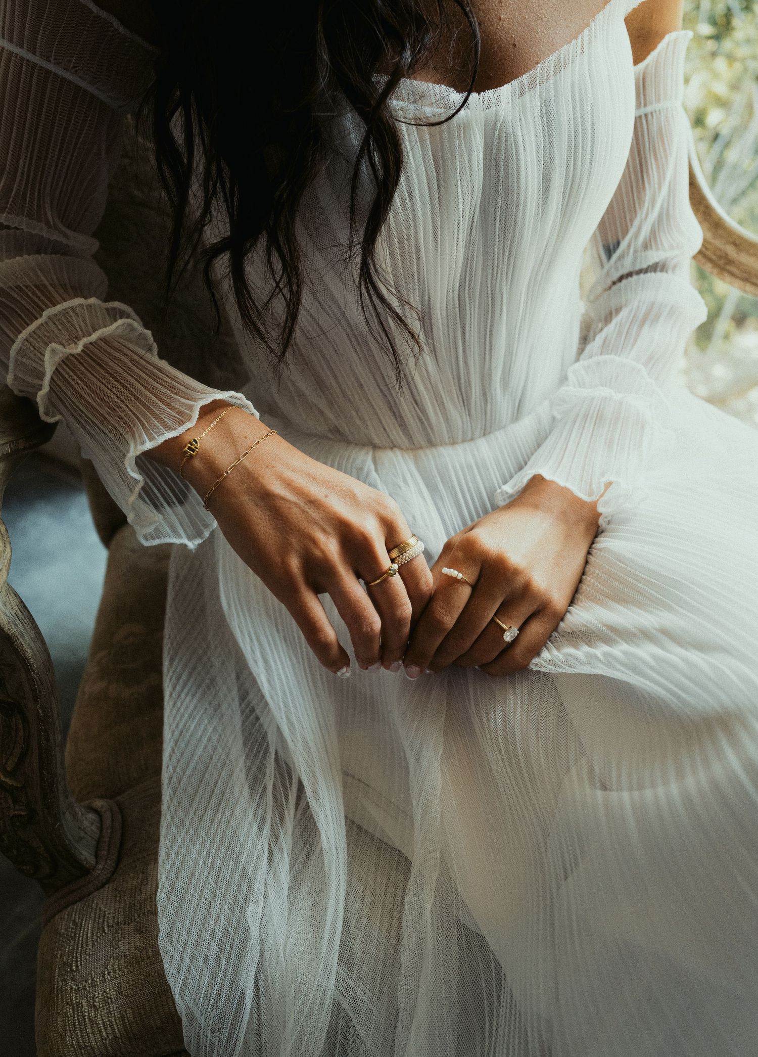 Close-up details of a delicate white dress with pleated fabric and hands gently touching the material.
