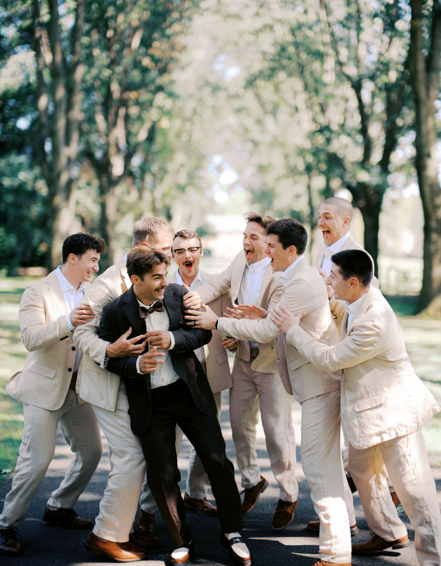 A sequence of groomsmen in light colored suits playfully posing and interacting in an outdoor wooded setting.