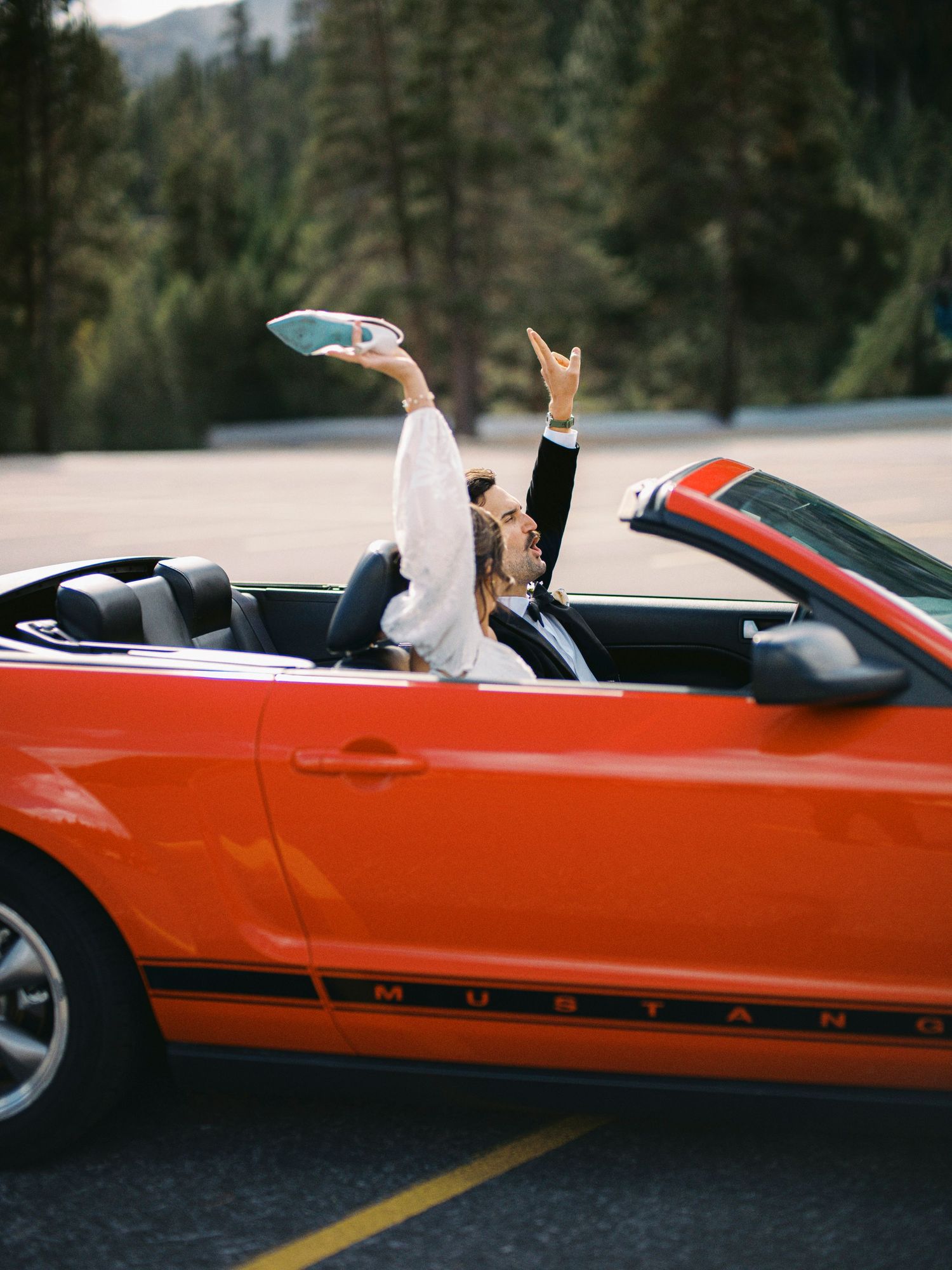 Playful couple having fun in a red convertible sports car against mountain backdrop.