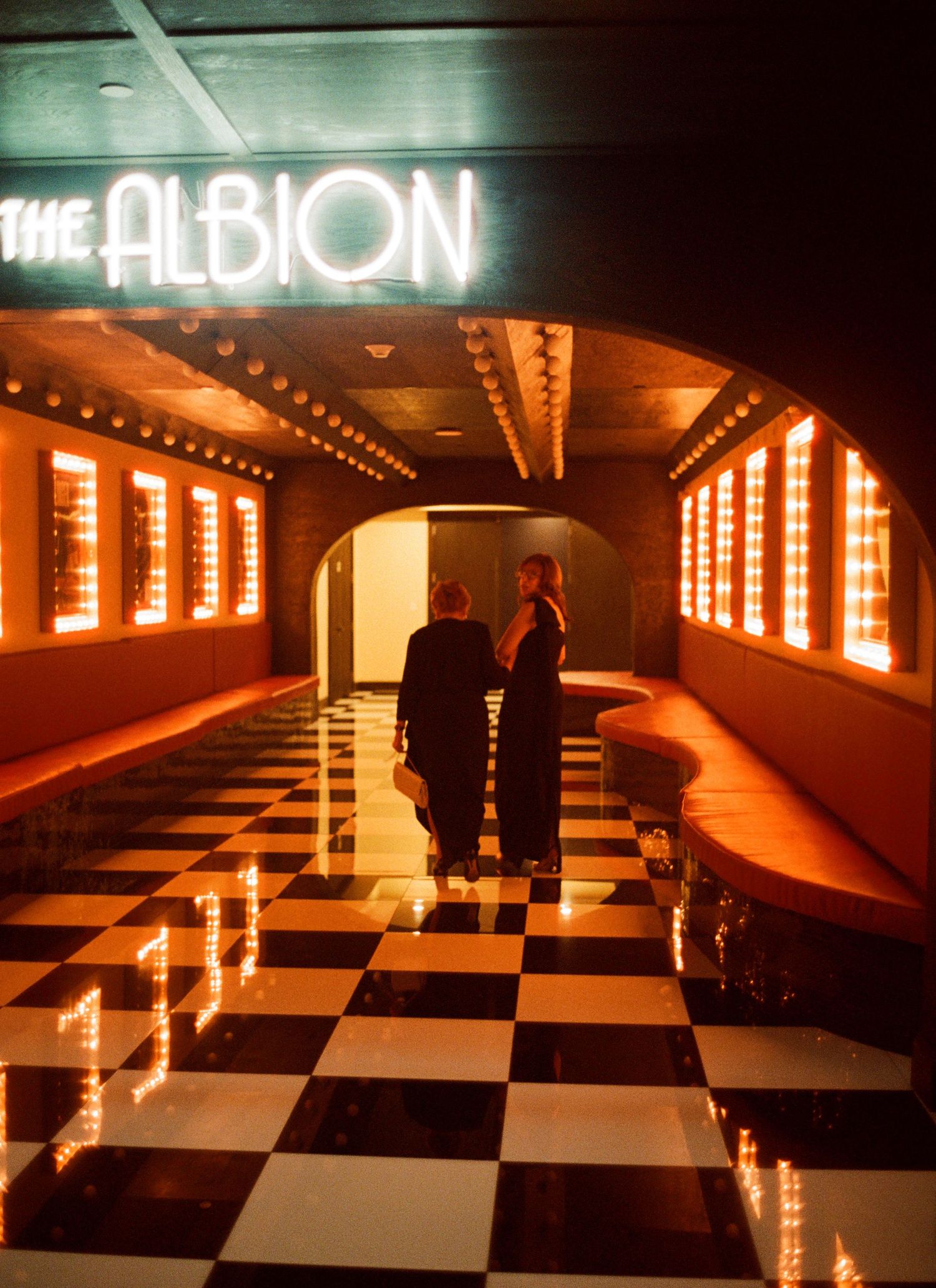 Checkered dance floor illuminated in warm orange lighting with mirrored walls creating a dramatic nightclub atmosphere.