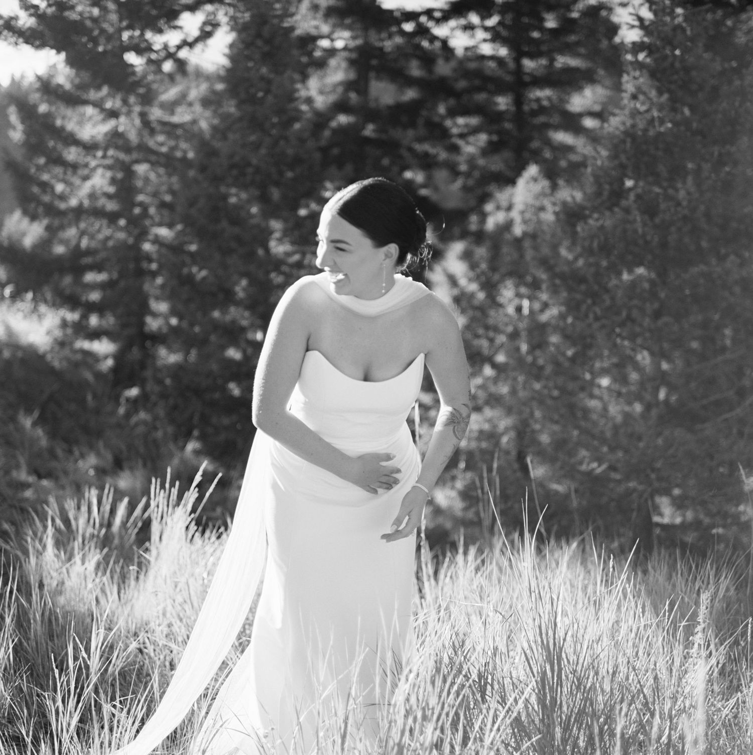 A person in a white dress runs through a sunlit field of tall grass creating a dreamy black and white scene.