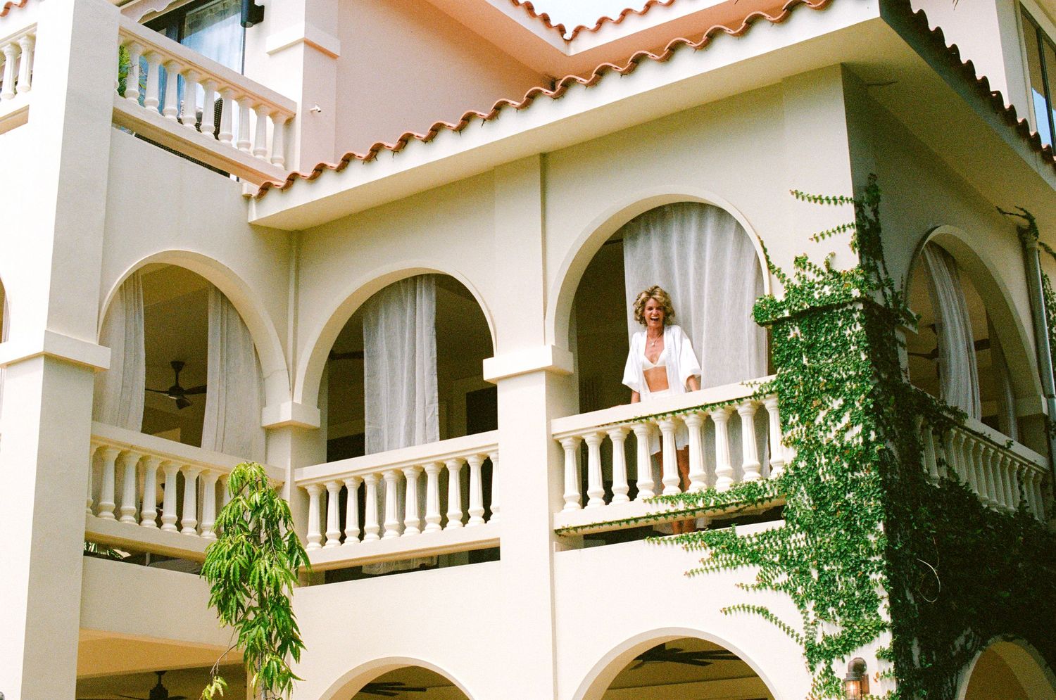 Mediterranean-style villa with white arched columns, terracotta roof tiles, and lush tropical landscaping.