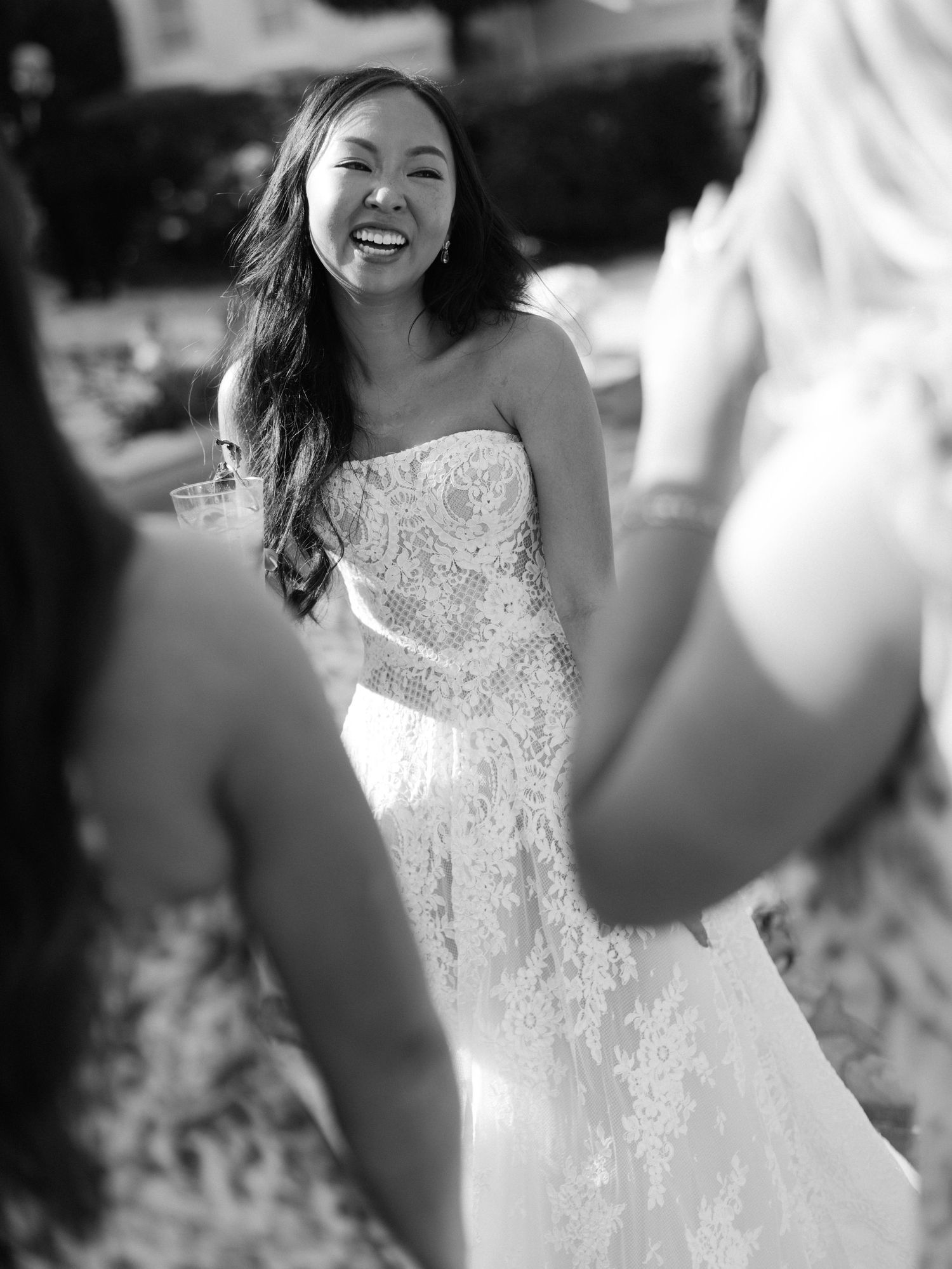 A joyful bride in a white lace wedding dress twirls and dances outdoors in a series of candid black and white photos.