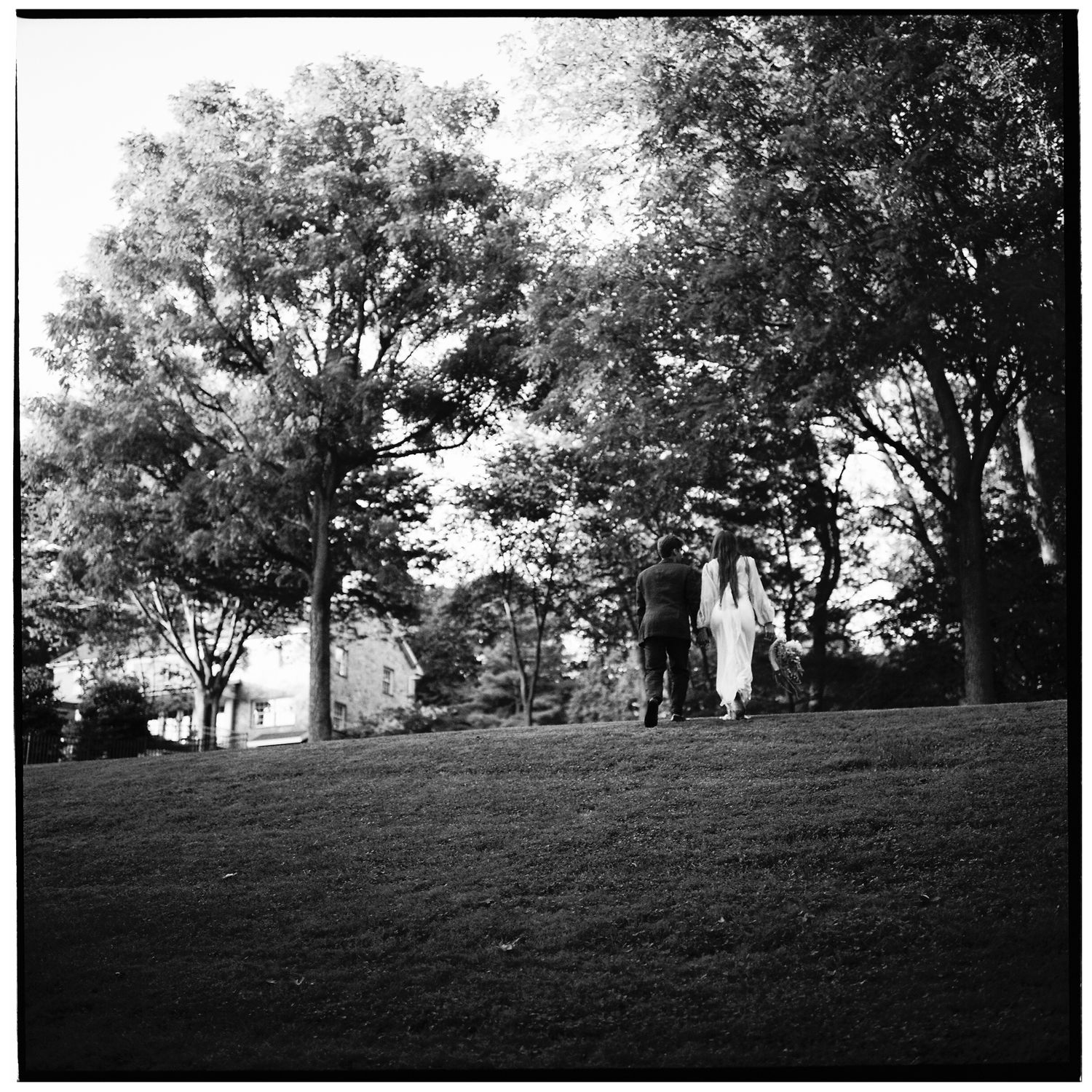Black and white image of figures walking on a hillside with trees.