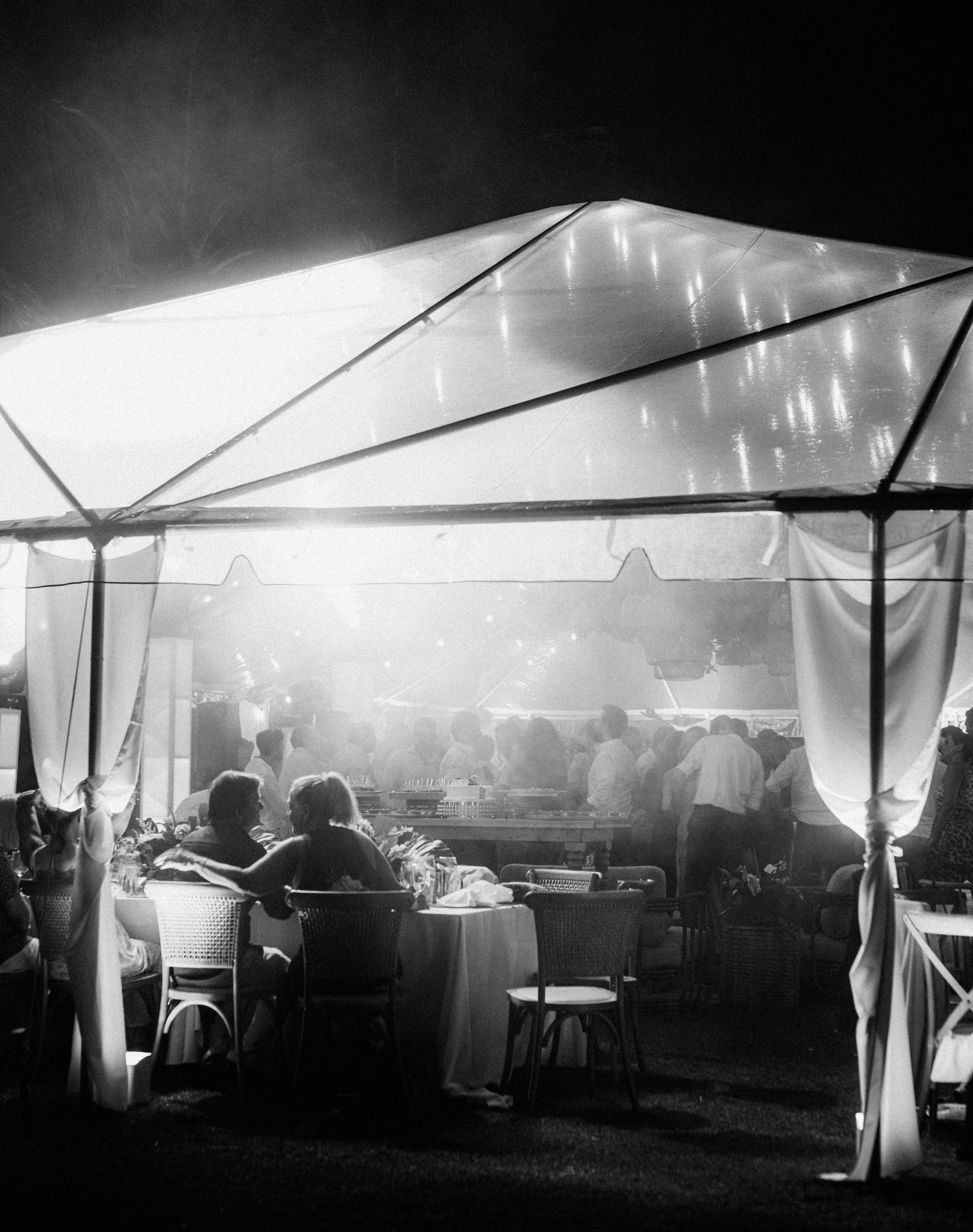 Silhouettes of people gathered under a large white tent at dusk with glowing lights creating an atmospheric ambiance.
