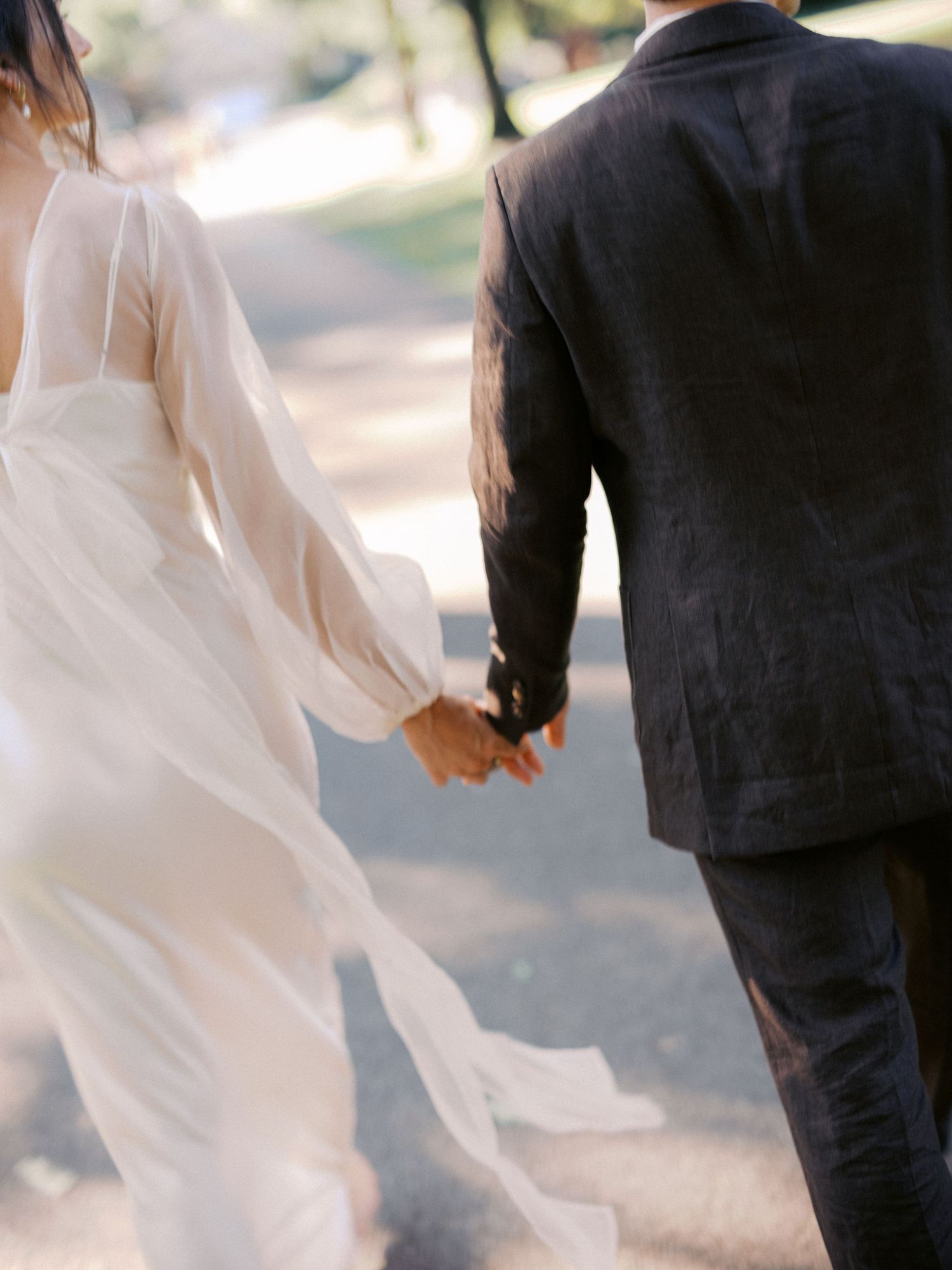 Romantic couple in wedding attire walking together with dress flowing in the breeze.