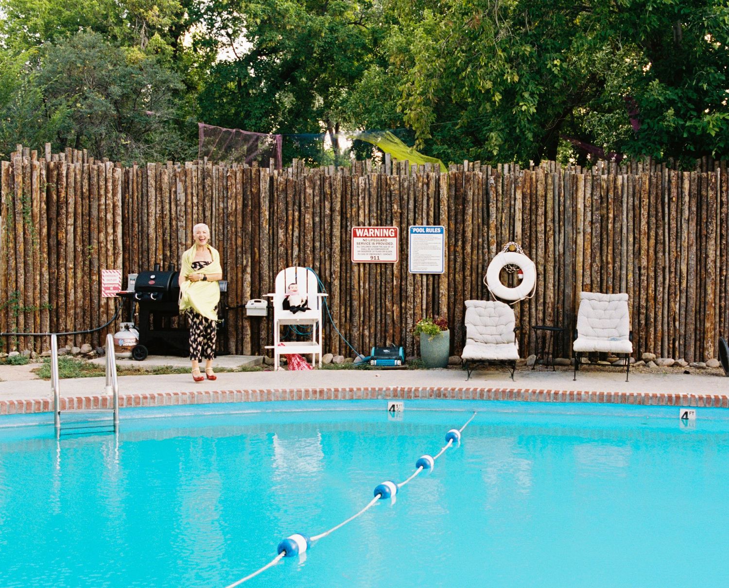 Bright turquoise swimming pool with lane dividers and wooden fence surrounds on a sunny summer day.