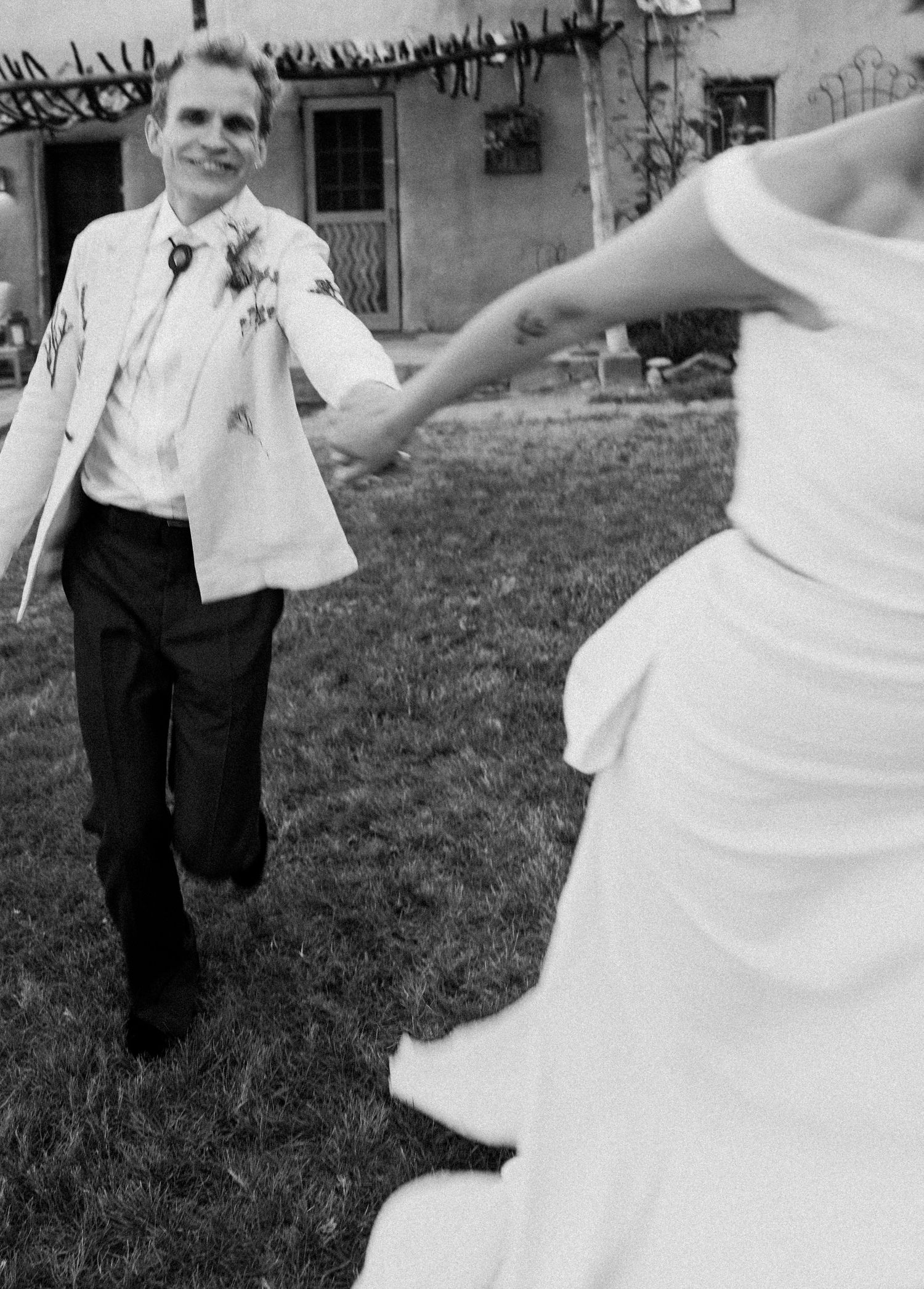 A joyful black and white wedding photo showing a couple dancing together on a lawn outside a house.