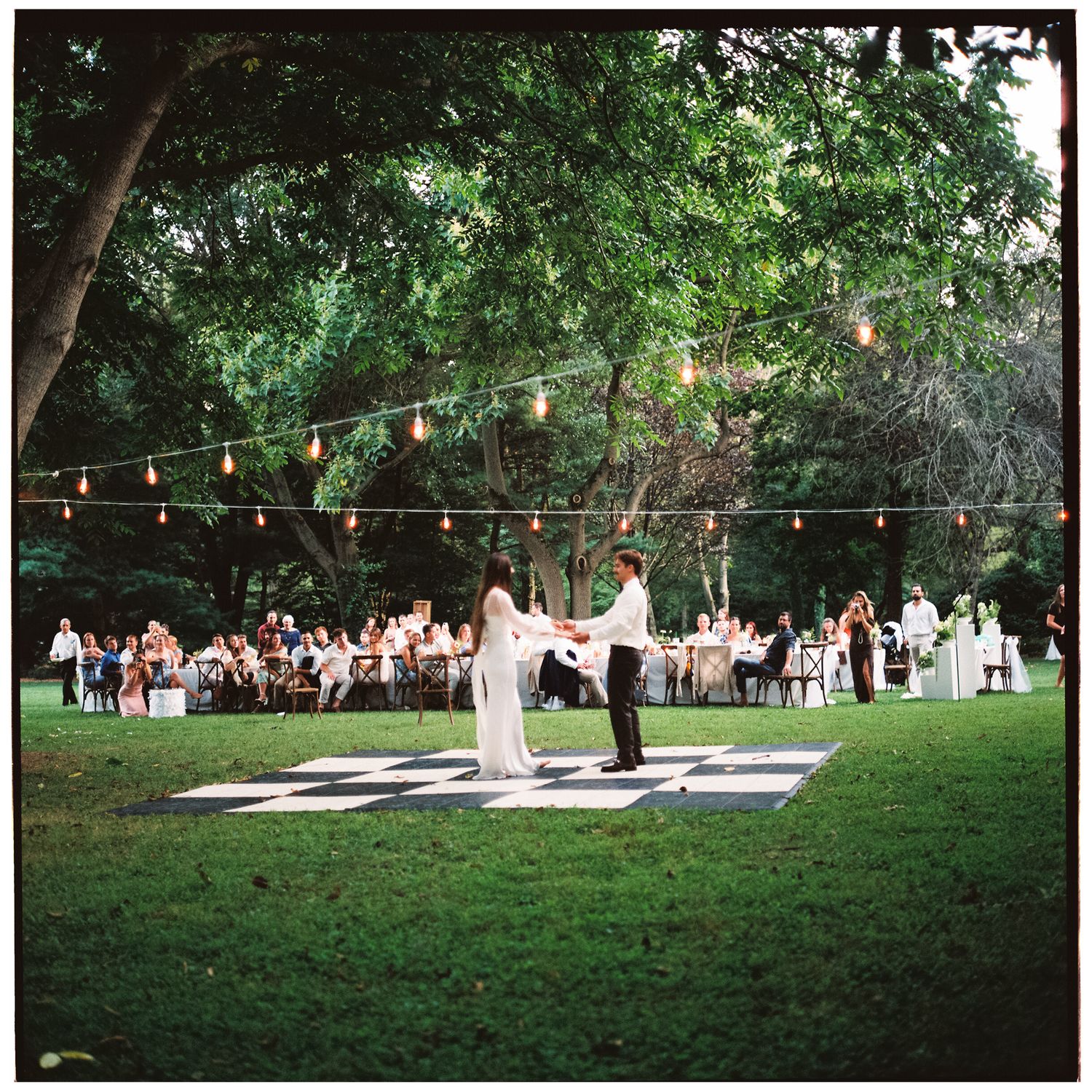 String lights illuminate an outdoor reception area with a checkered dance floor.