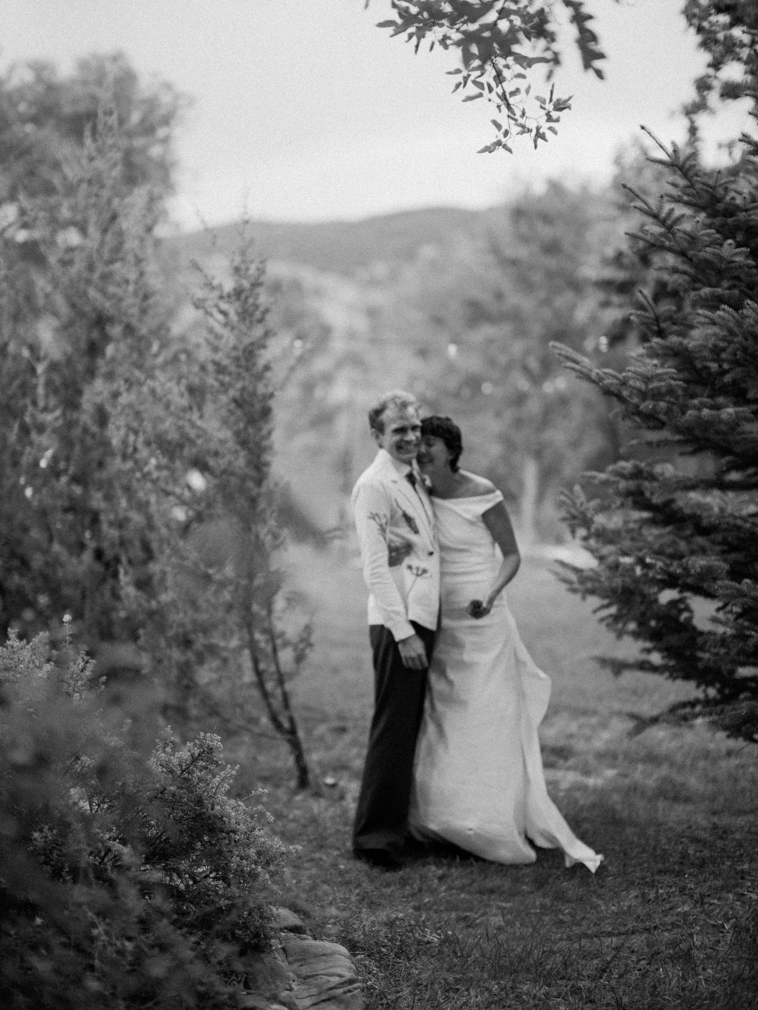 Romantic black and white photo series of a couple in elegant attire posing together among evergreen trees in nature.