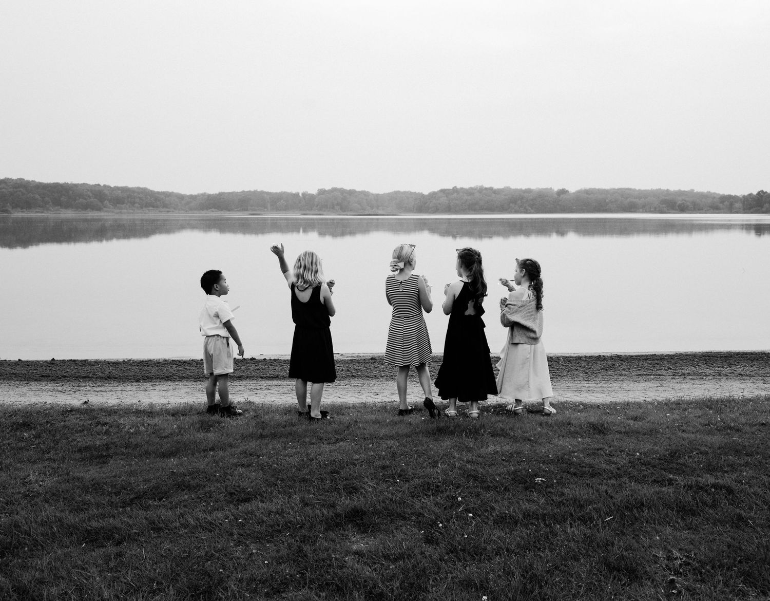 Silhouettes of wedding party standing against waterfront landscape.